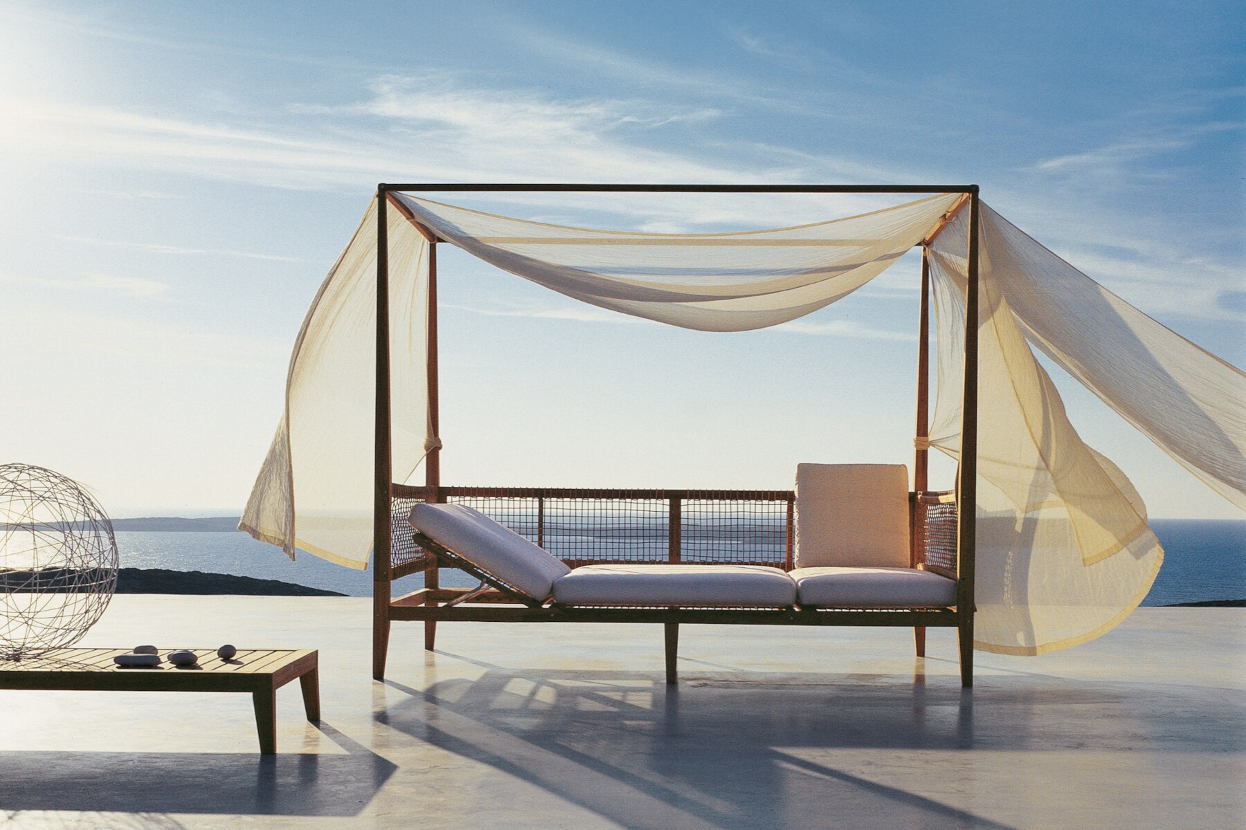 Himmelbett mit im Wind wehenden Vorhängen auf einer Terrasse am Meer