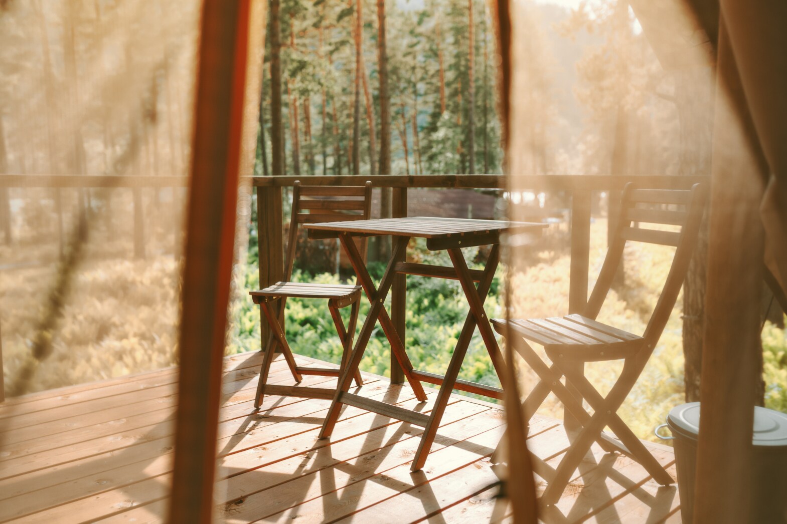 Blick auf eine Holzterrasse mit Stühlen und Tisch, im Hintergrund Wald