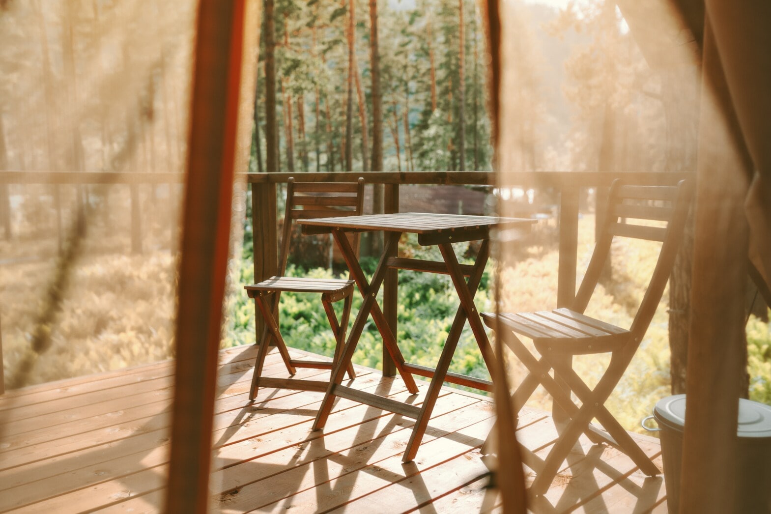 Blick auf eine Holzterrasse mit Stühlen und Tisch, im Hintergrund Wald Blick auf eine Holzterrasse mit Stühlen und Tisch, im Hintergrund Wald
