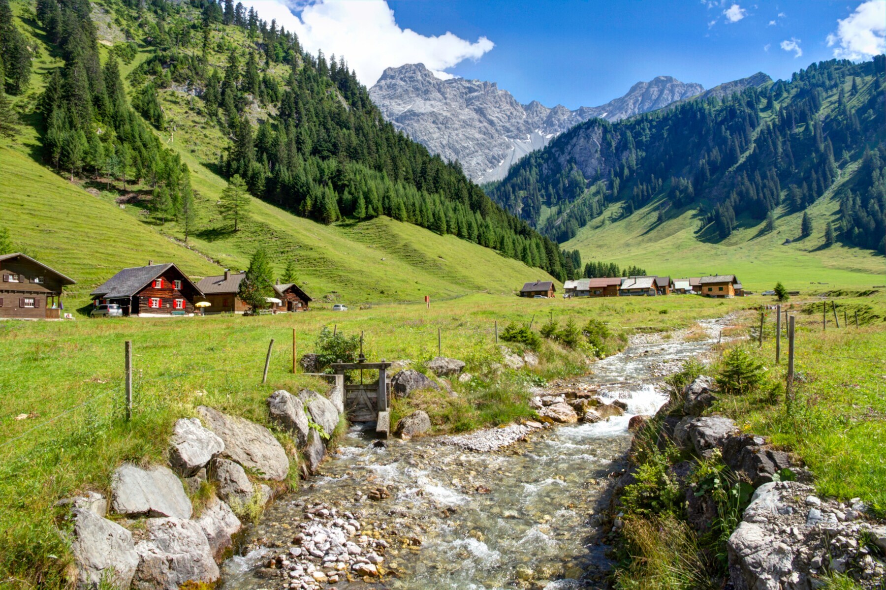 Holzhütten am Fuße der Alpen mit einem Bachlauf davor