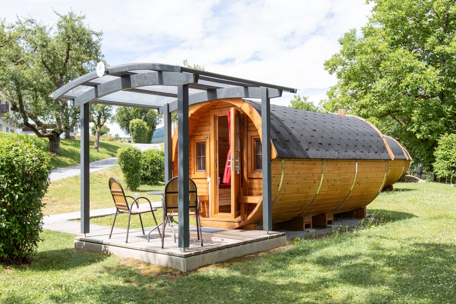 Ein zum Schlafplatz umgebautes Holzfass auf einer Wiese mit zwei Stühlen davor