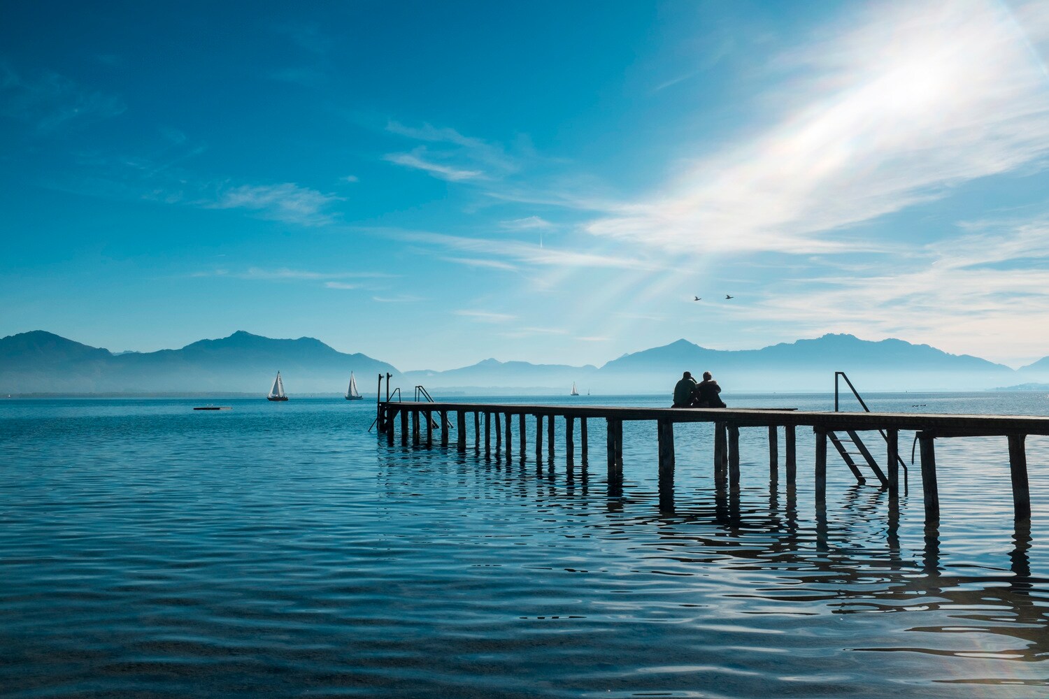 Zwei Personen sitzen auf einem Holzsteg auf dem Chiemsee
