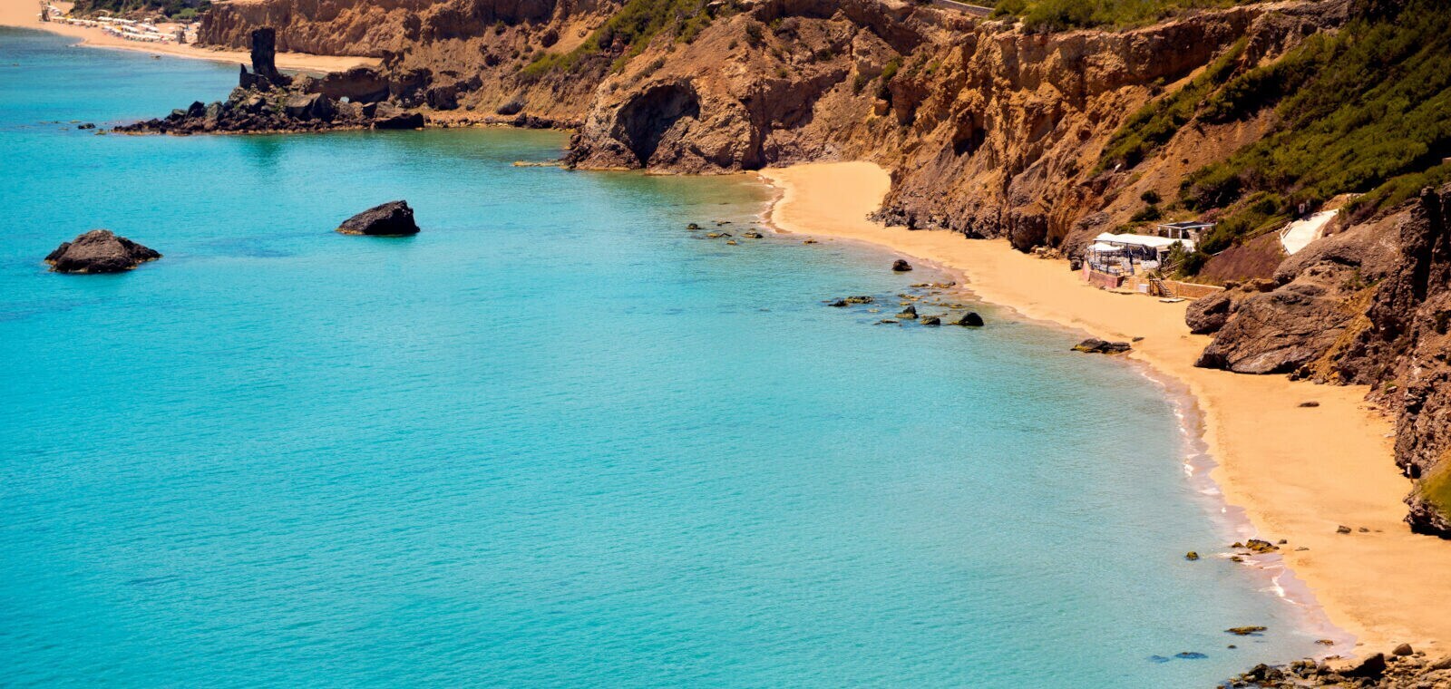 Eine kleine, felsige Bucht mit Sandstrand und Strandkiosk am türkisblauen Meer