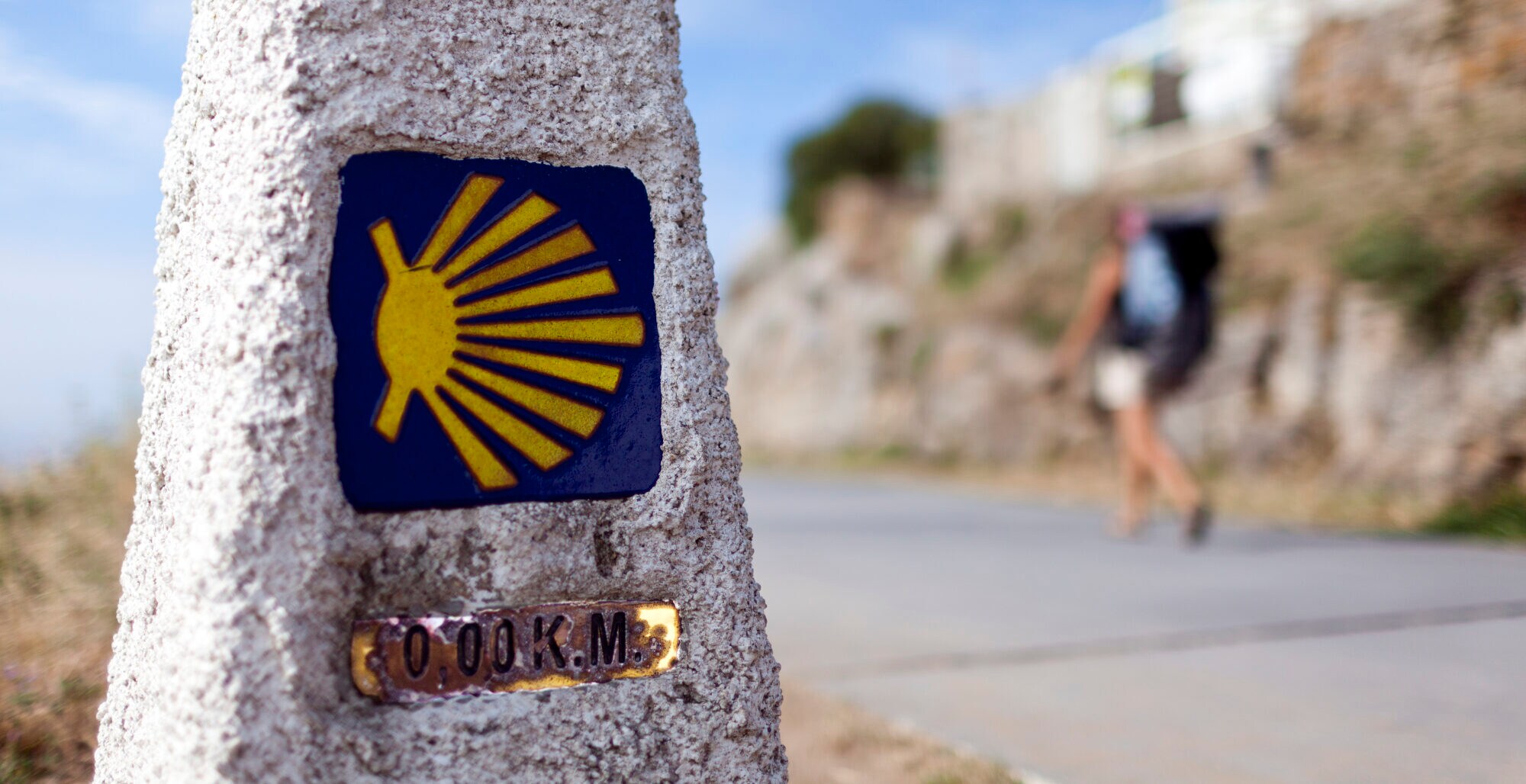 Wegmarkierung mit Wanderer im Hintergrund
