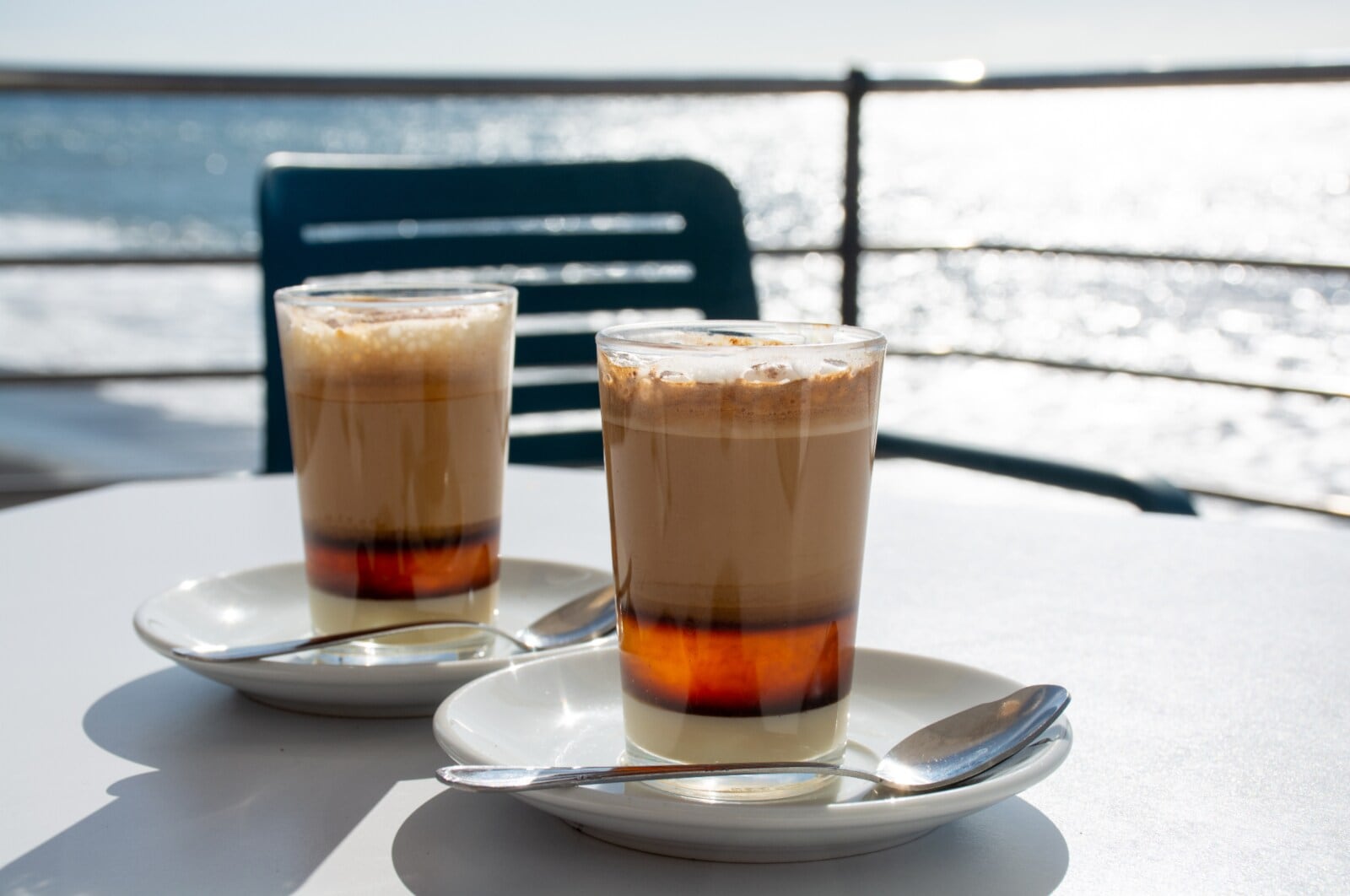 Zwei Gläser mit Barraquito auf einem Tisch mit dem Meer im Hintergrund Zwei Gläser mit Barraquito auf einem Tisch mit dem Meer im Hintergrund