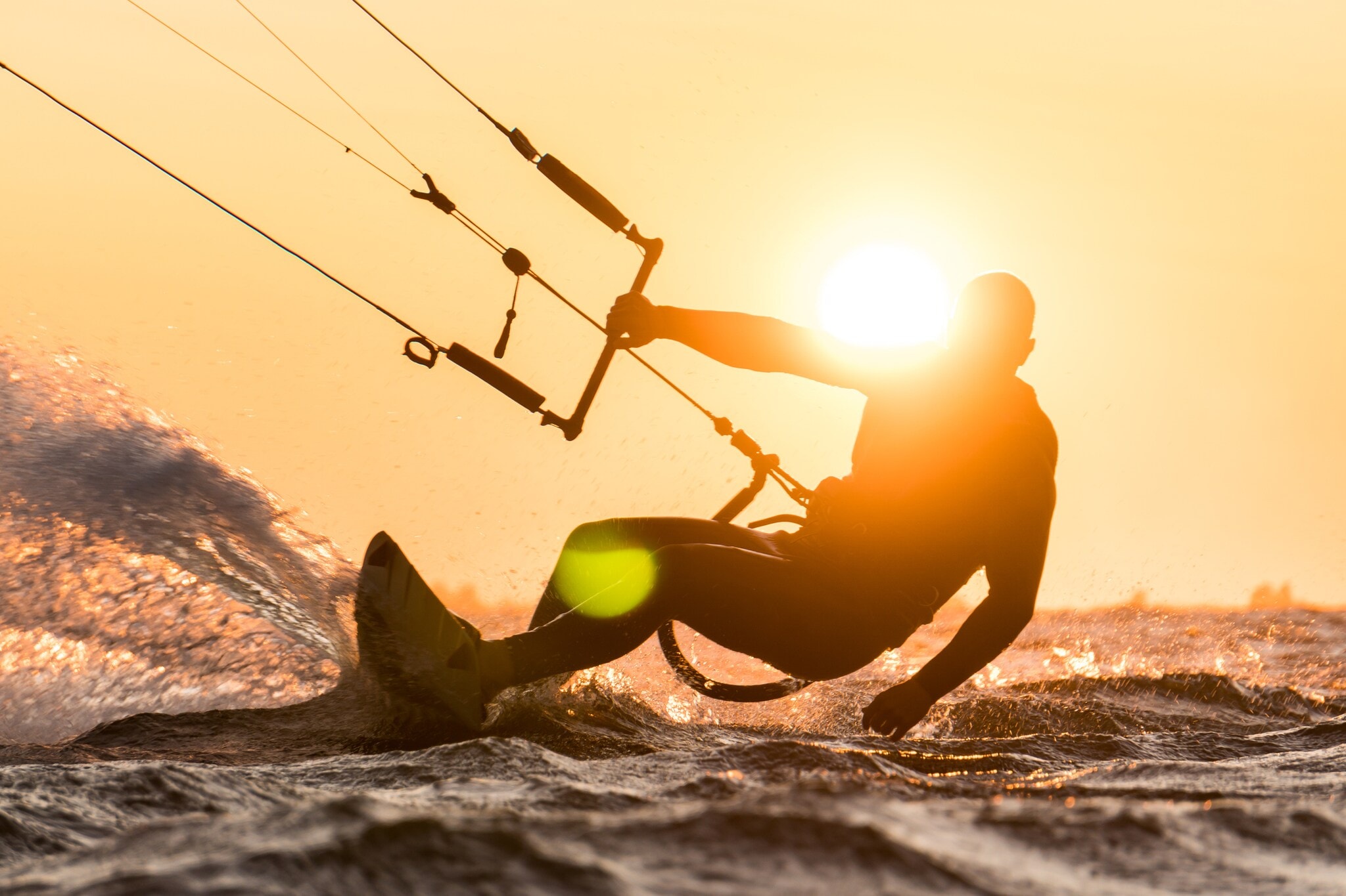 Silhouette des Kitesurfers, der bei schönem Sonnenuntergang mit Sonne neben dem Fahrerkopf reitet Silhouette des Kitesurfers, der bei schönem Sonnenuntergang mit Sonne neben dem Fahrerkopf reitet