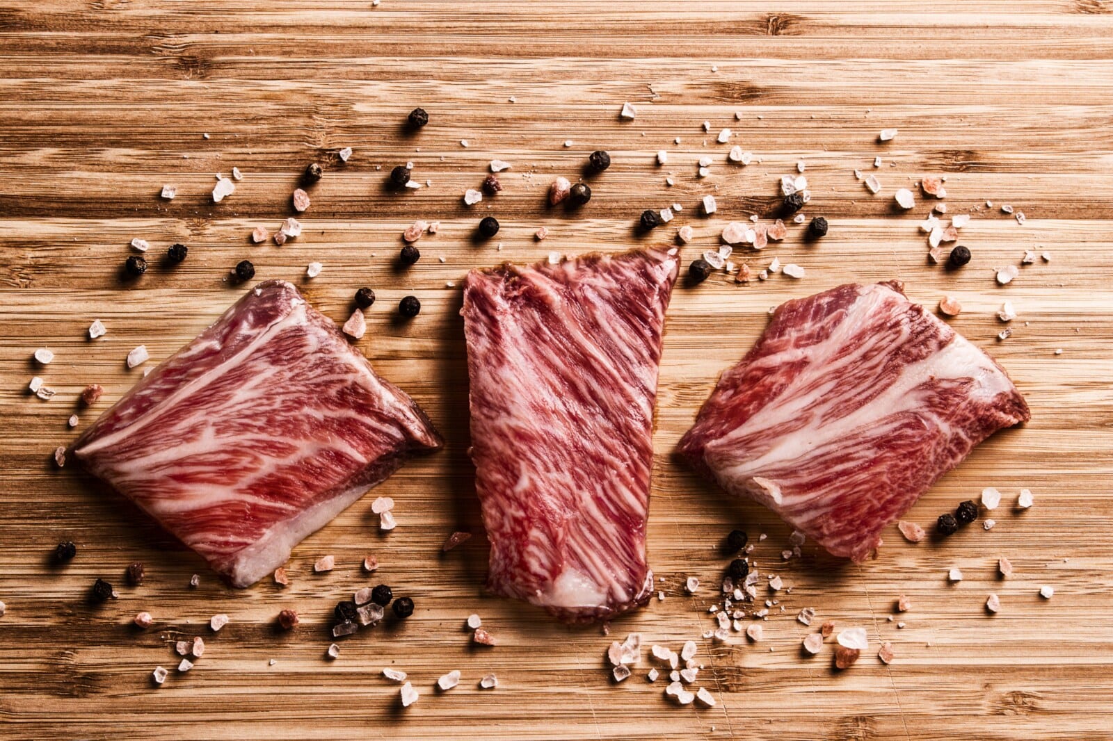 Drei Kobe-Rind-Stücke auf Holz mit Pfeffer und Salz
