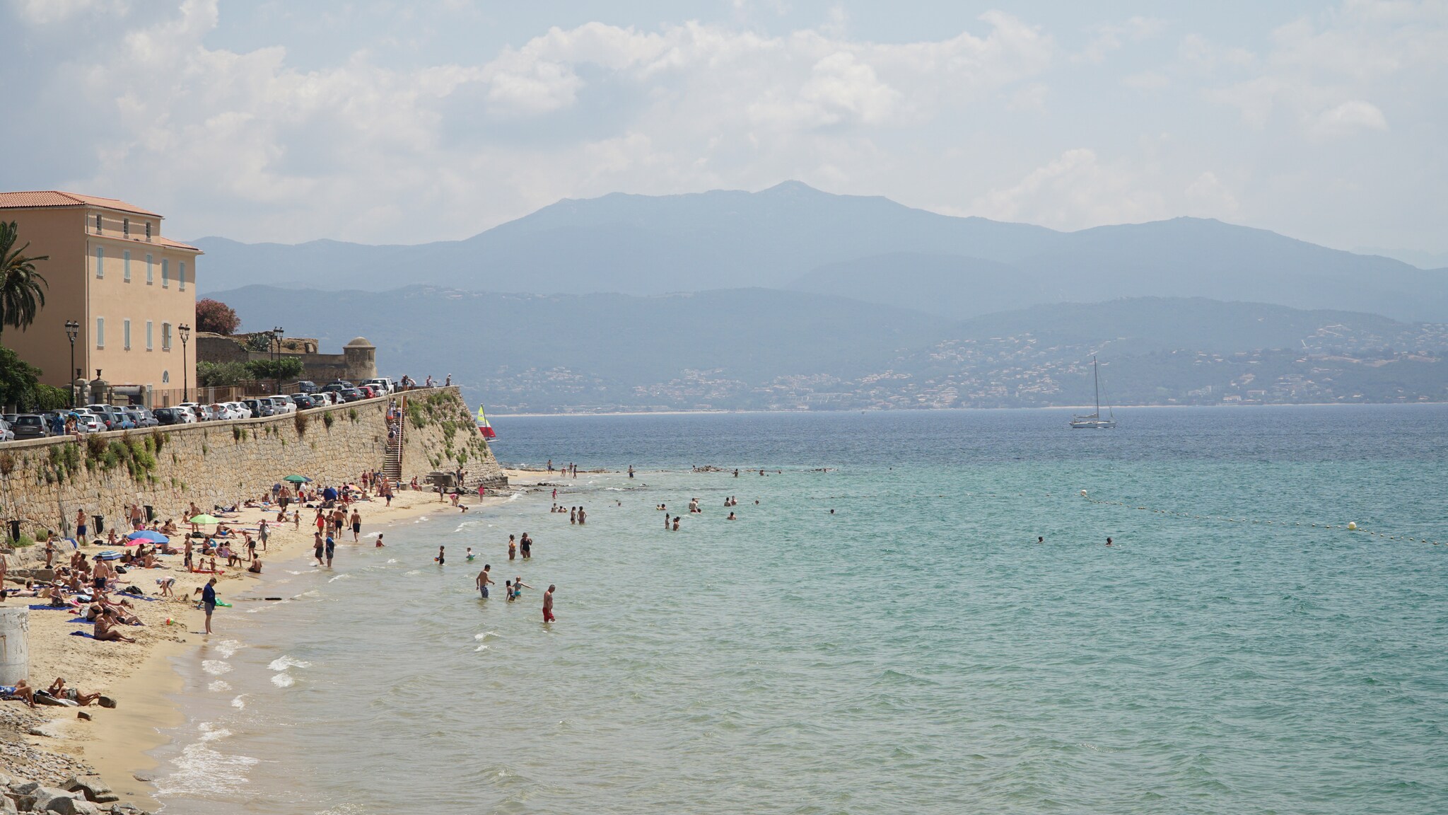 Ein Strandabschnitt mit badenden Menschen, im Hintergrund bergige Landschaft