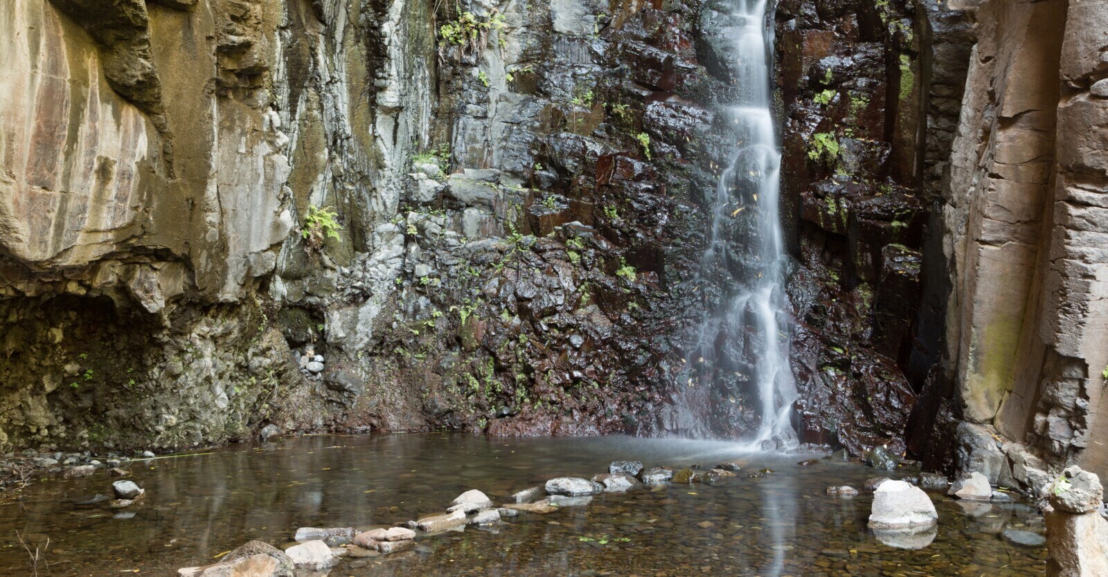 Ein kleinerer Wasserfall, der zwischen Felswänden herabfällt und in einem kleinen Teich endet