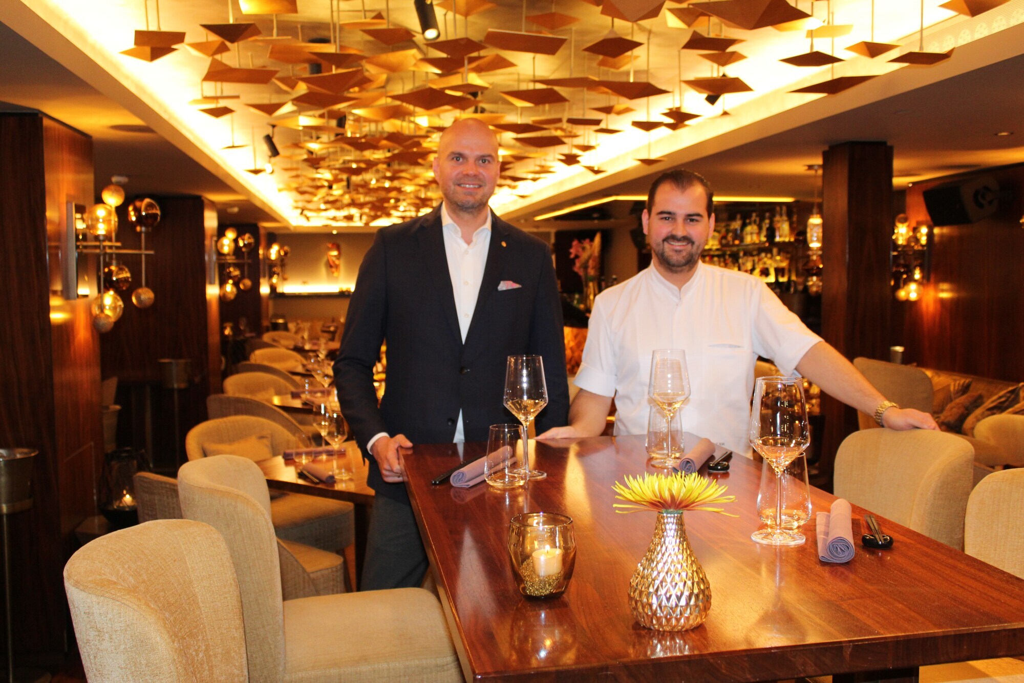 Zwei Personen stehen an einem dezent gedeckten Tisch in einem Restaurant Zwei Personen stehen an einem dezent gedeckten Tisch in einem Restaurant