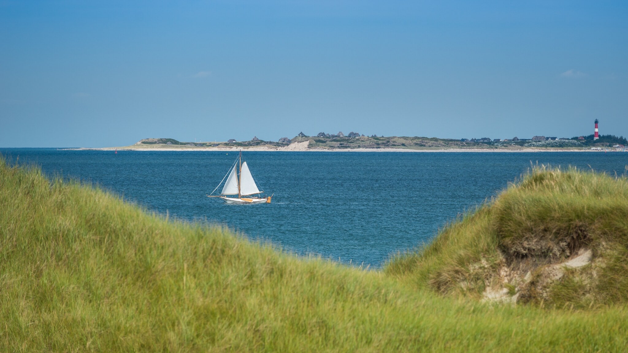 Blick durch die Dünenlandschaft aufs Meer, auf dem ein Segelboot fährt Blick durch die Dünenlandschaft aufs Meer, auf dem ein Segelboot fährt