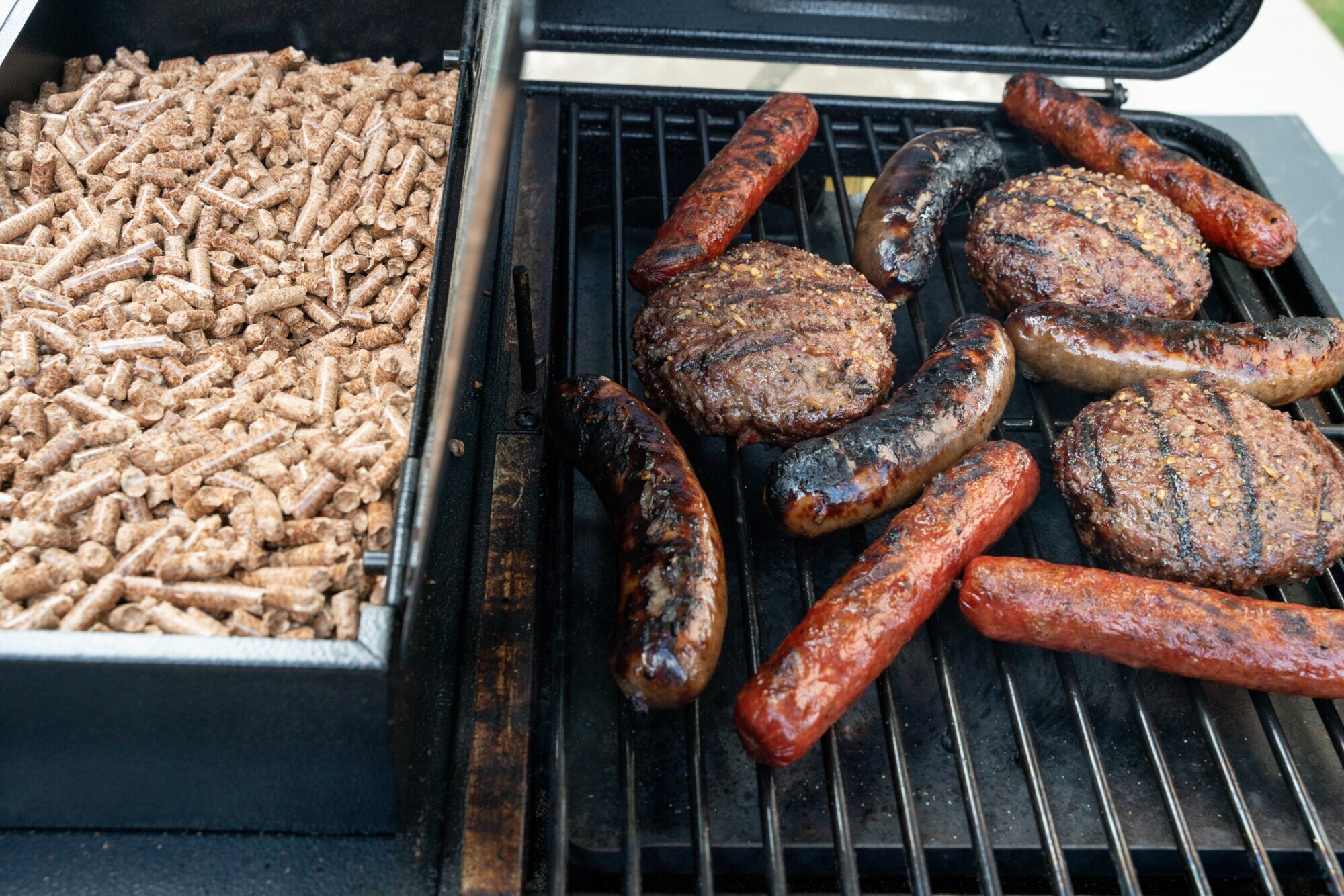 Bratwurst und Buletten auf einem Rost neben einer Schale mit Pellets