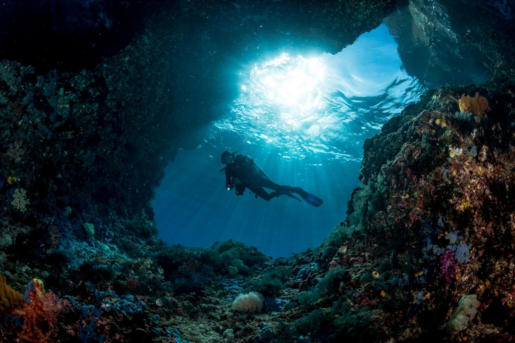 Taucher unter Wasser am Eingang einer Höhle mit Sonnenstrahlen im Hintergrund Taucher unter Wasser am Eingang einer Höhle mit Sonnenstrahlen im Hintergrund