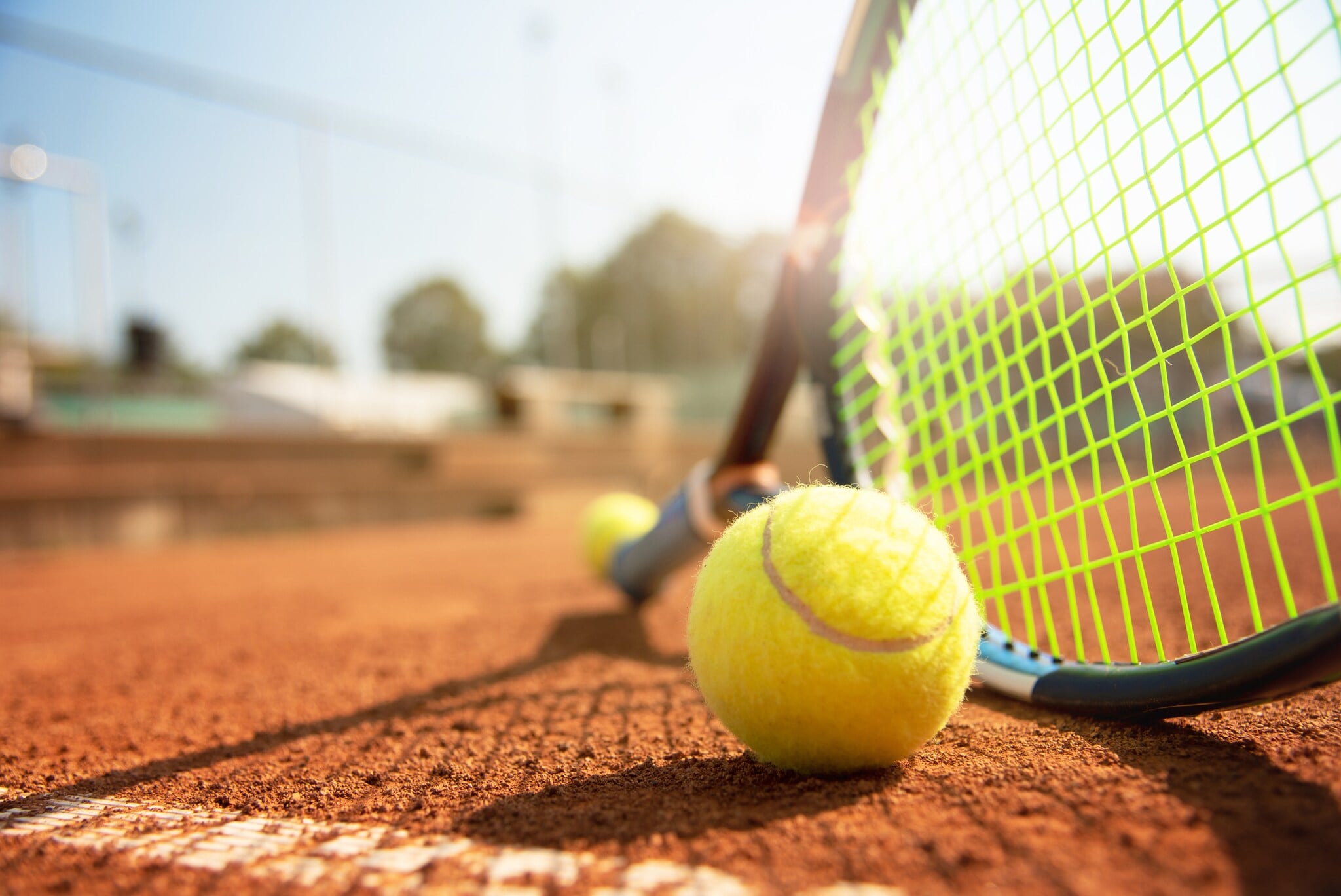 Tennisball und Schläger auf einem Tennisplatz bei schönem Wetter Tennisball und Schläger auf einem Tennisplatz bei schönem Wetter