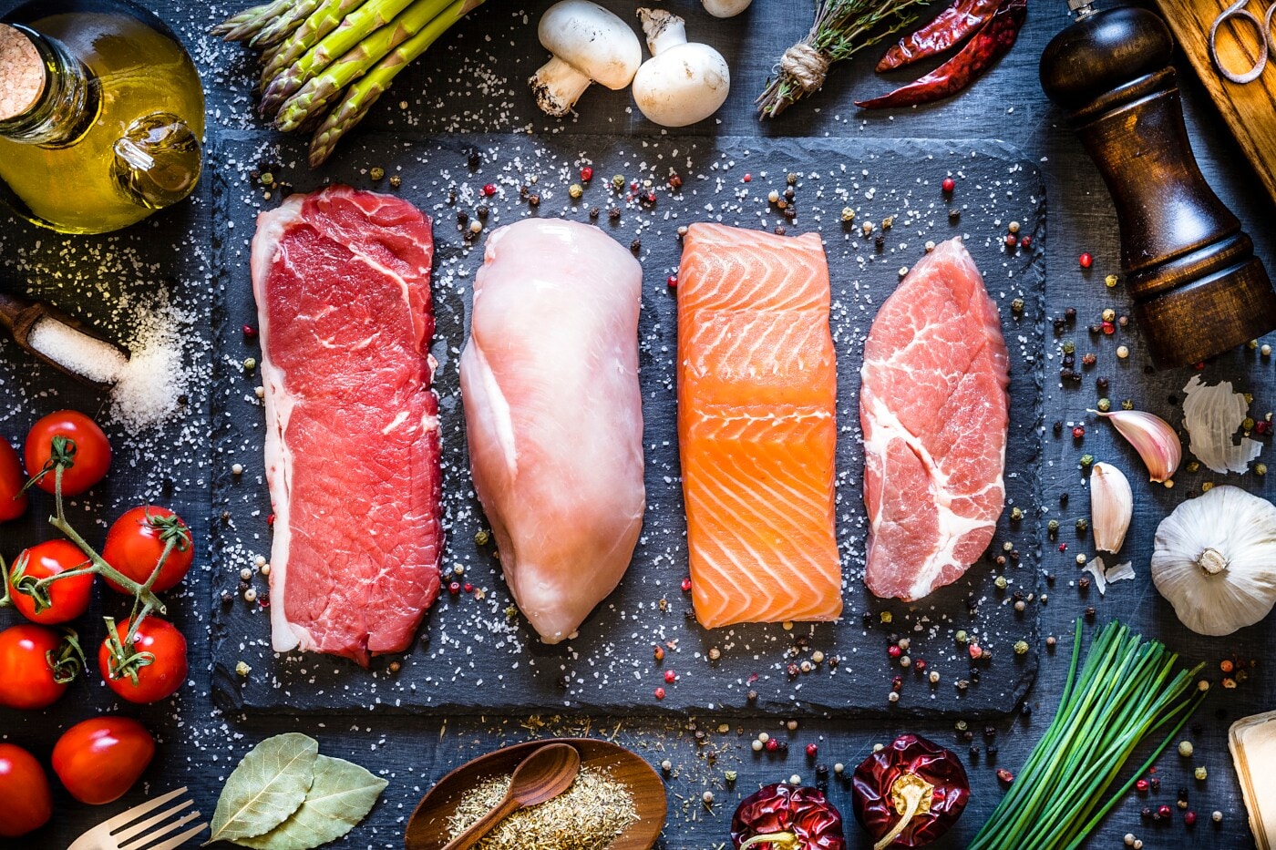 Stücke von unterschiedlichem tierischem Fleisch nebeneinander, garniert mit Gewürzen und Öl Stücke von unterschiedlichem tierischem Fleisch nebeneinander, garniert mit Gewürzen und Öl