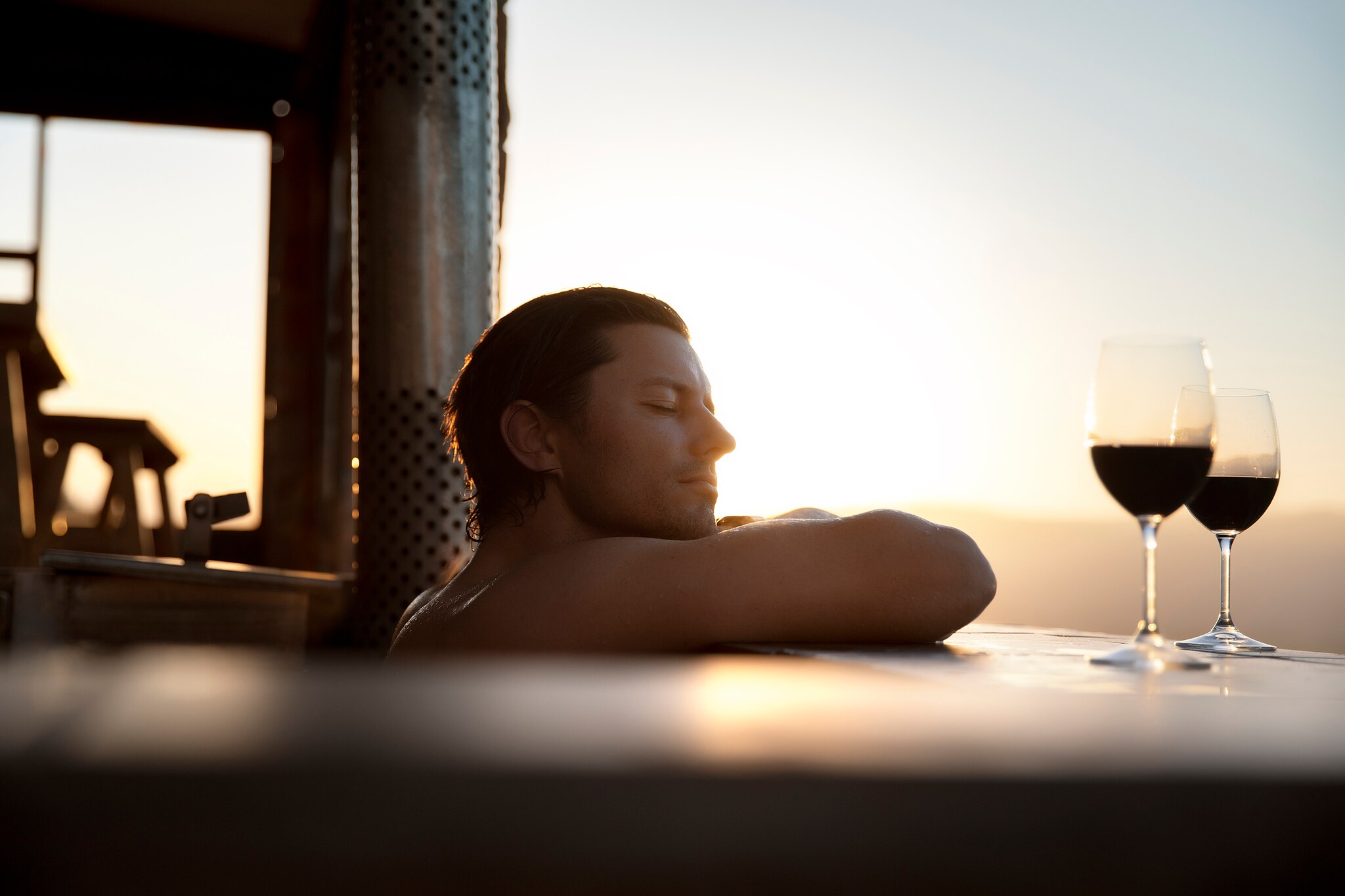 Ein Mann genießt im Whirlpool die Abendsonne bei zwei Gläsern Wein