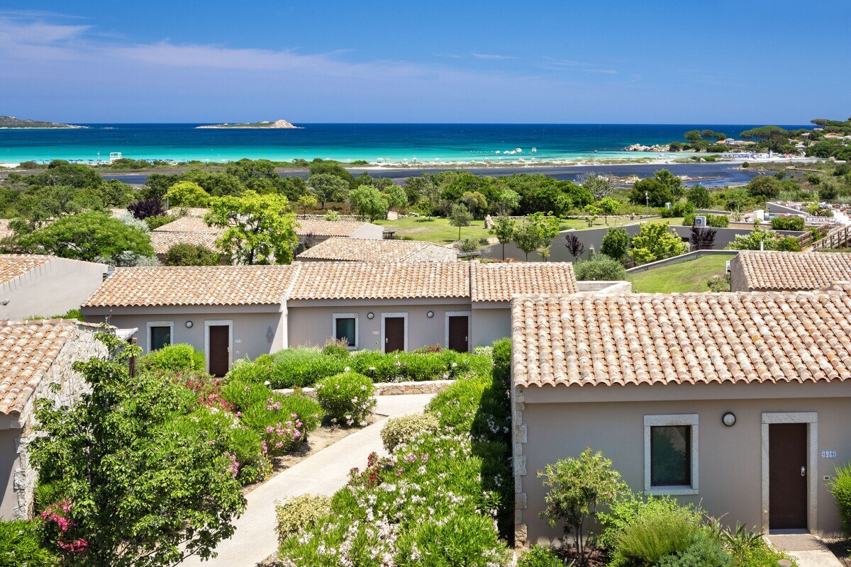 Kleiner Häuschen in einer parkähnlichen Anlage vor einem türkisfarbenen Meer