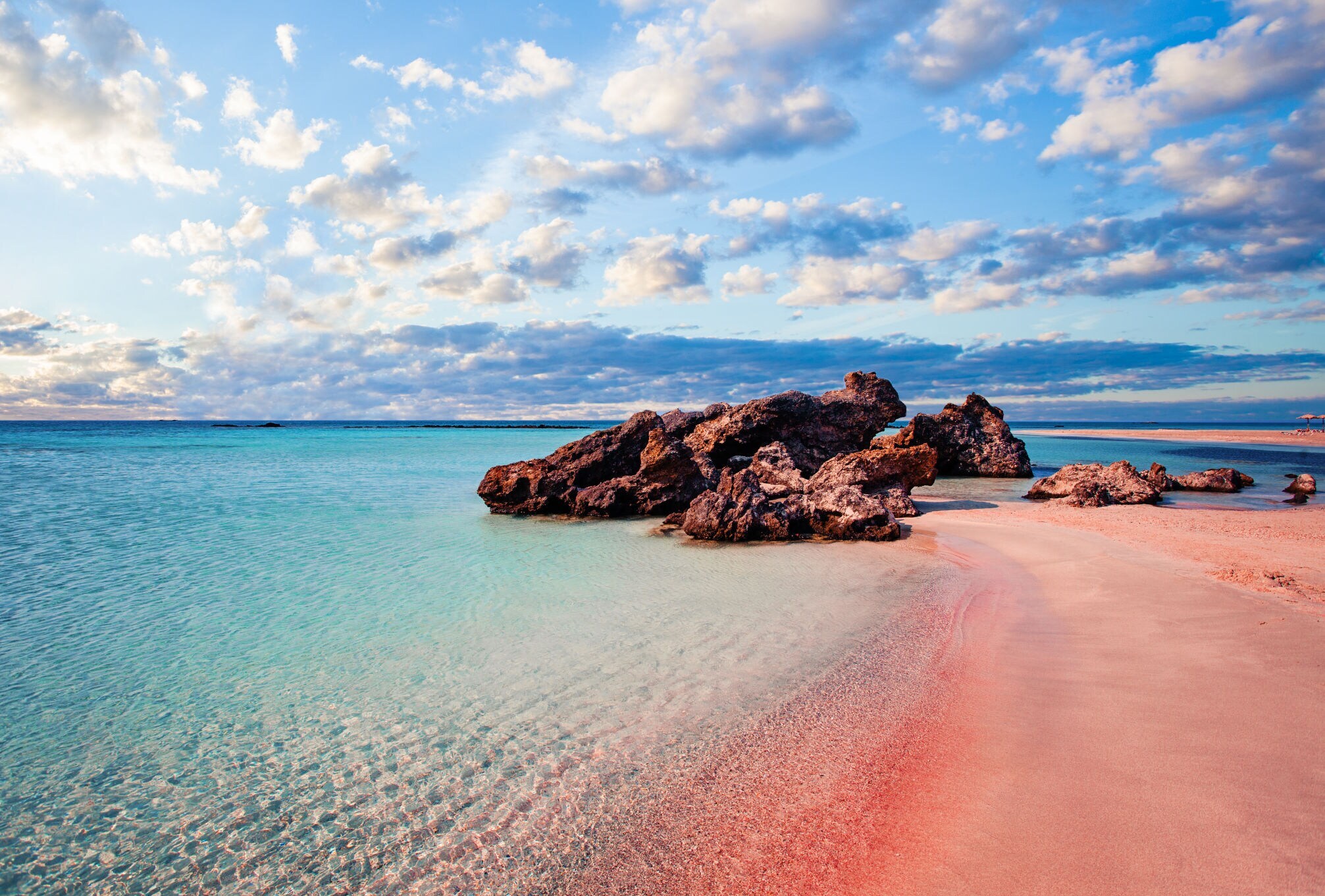 Ein Strand mit rosa Sand und Felsen im türkisblauen Wasser.