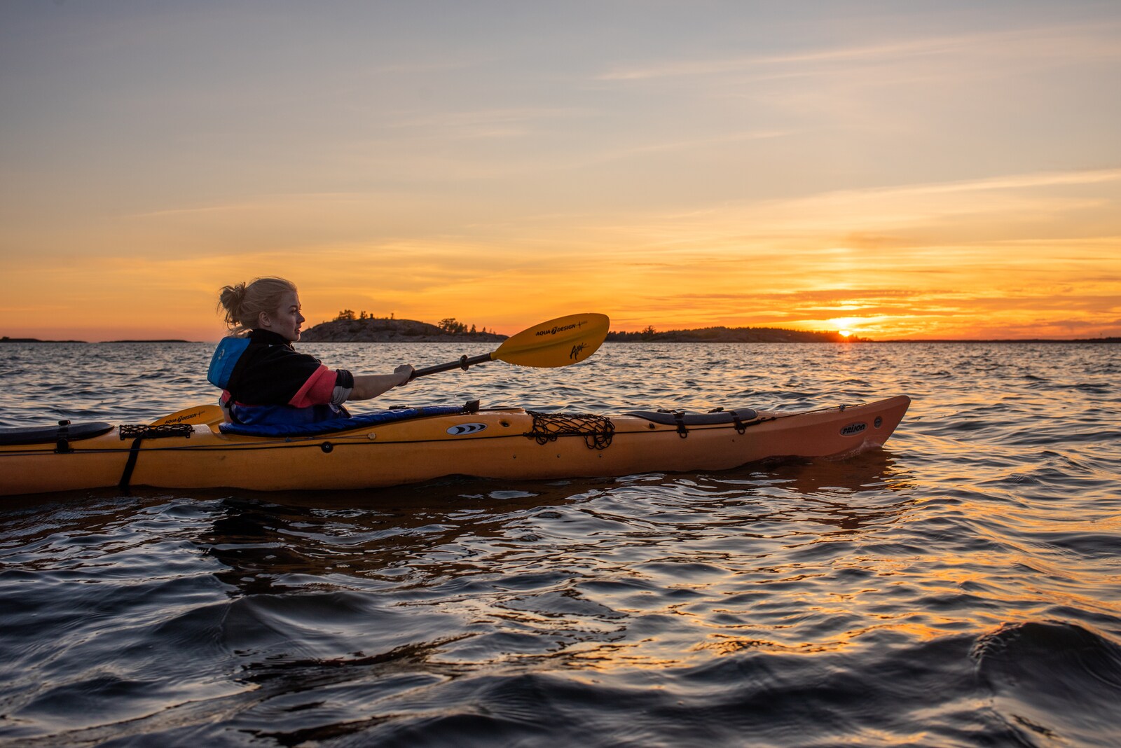 Eine Frau in einem Kajak auf einem Gewässer bei Sonnenuntergang