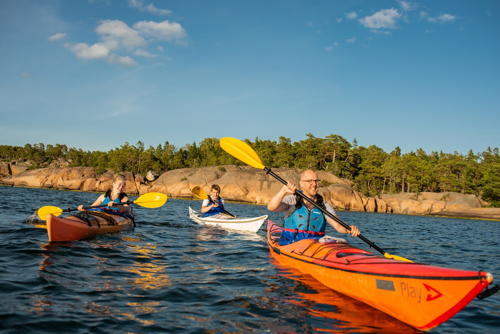 Eine Familie in Kajaks auf dem Wasser, im Hintergrund eine felsige Küste
