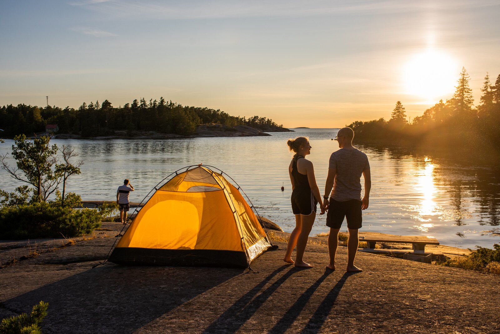 Drei Personen und ein Zelt an einem Gewässer in der Abendsonne
