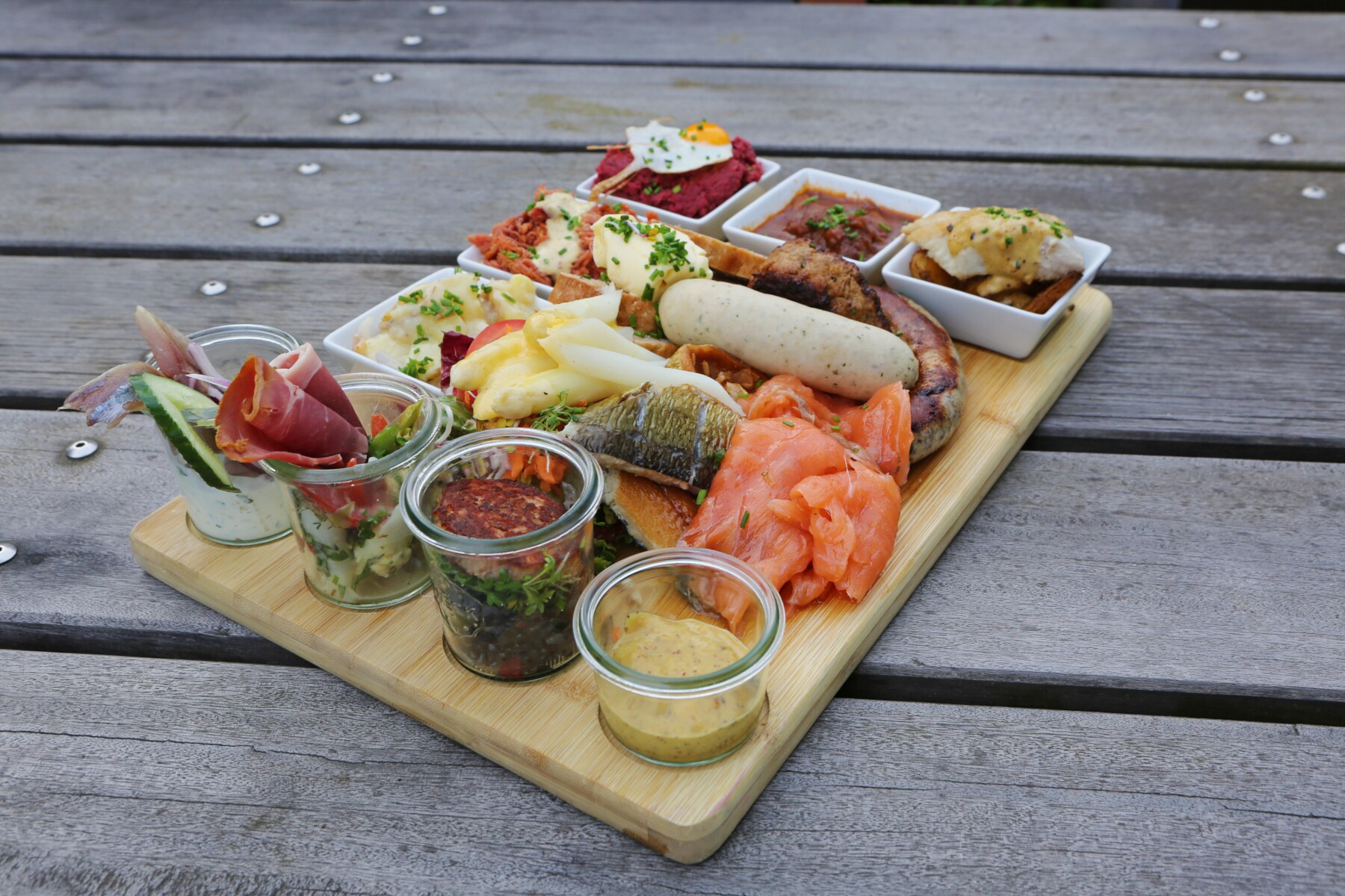 Ein Holzteller mit Fisch, Weißwurst, Labskaus und anderen leckeren Kleinigkeiten