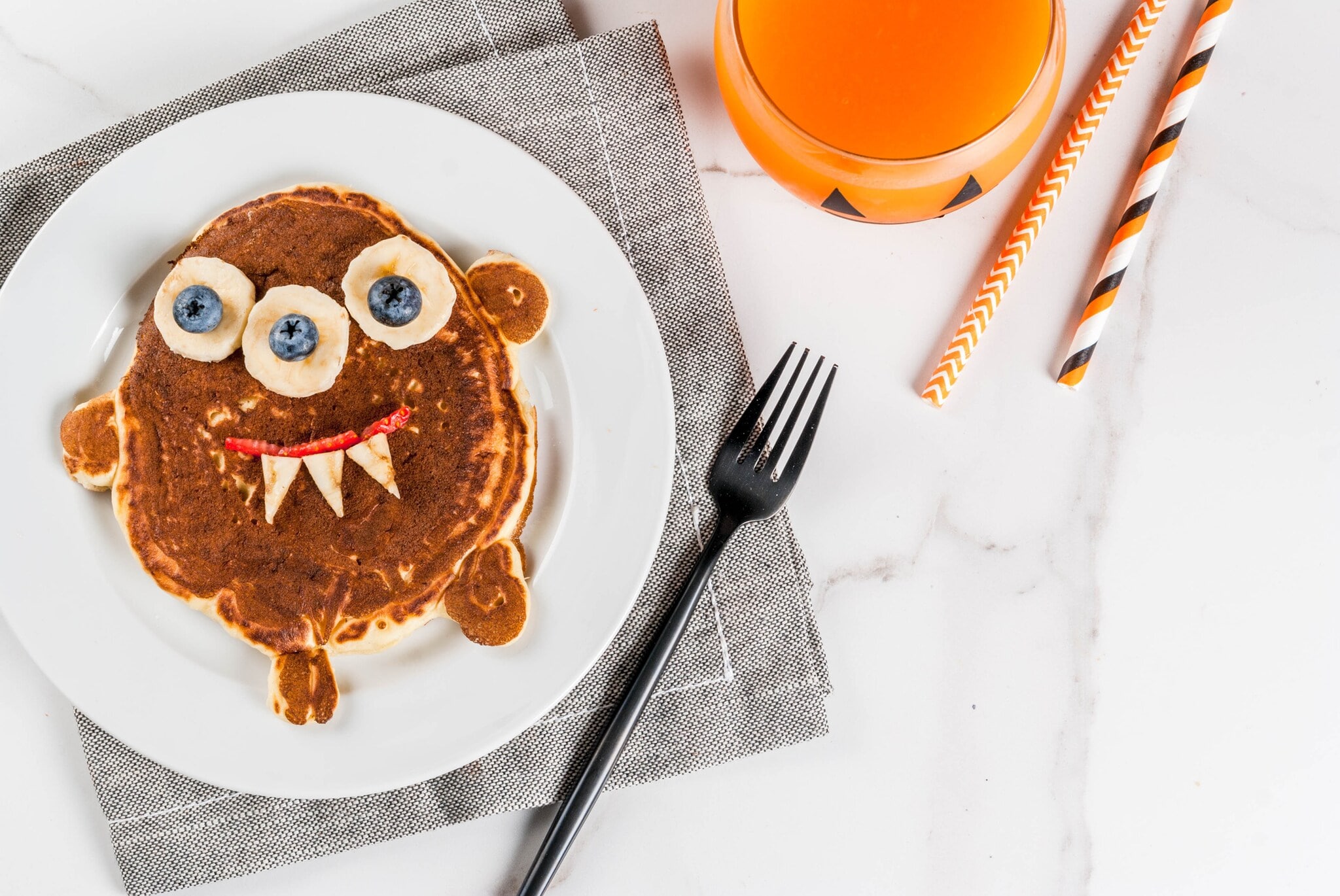 Frühstücksteller mit einem Pancake in Form eines kleinen Monsters, dessen Augen aus Bananen und Blaubeeren bestehen Frühstücksteller mit einem Pancake in Form eines kleinen Monsters, dessen Augen aus Bananen und Blaubeeren bestehen