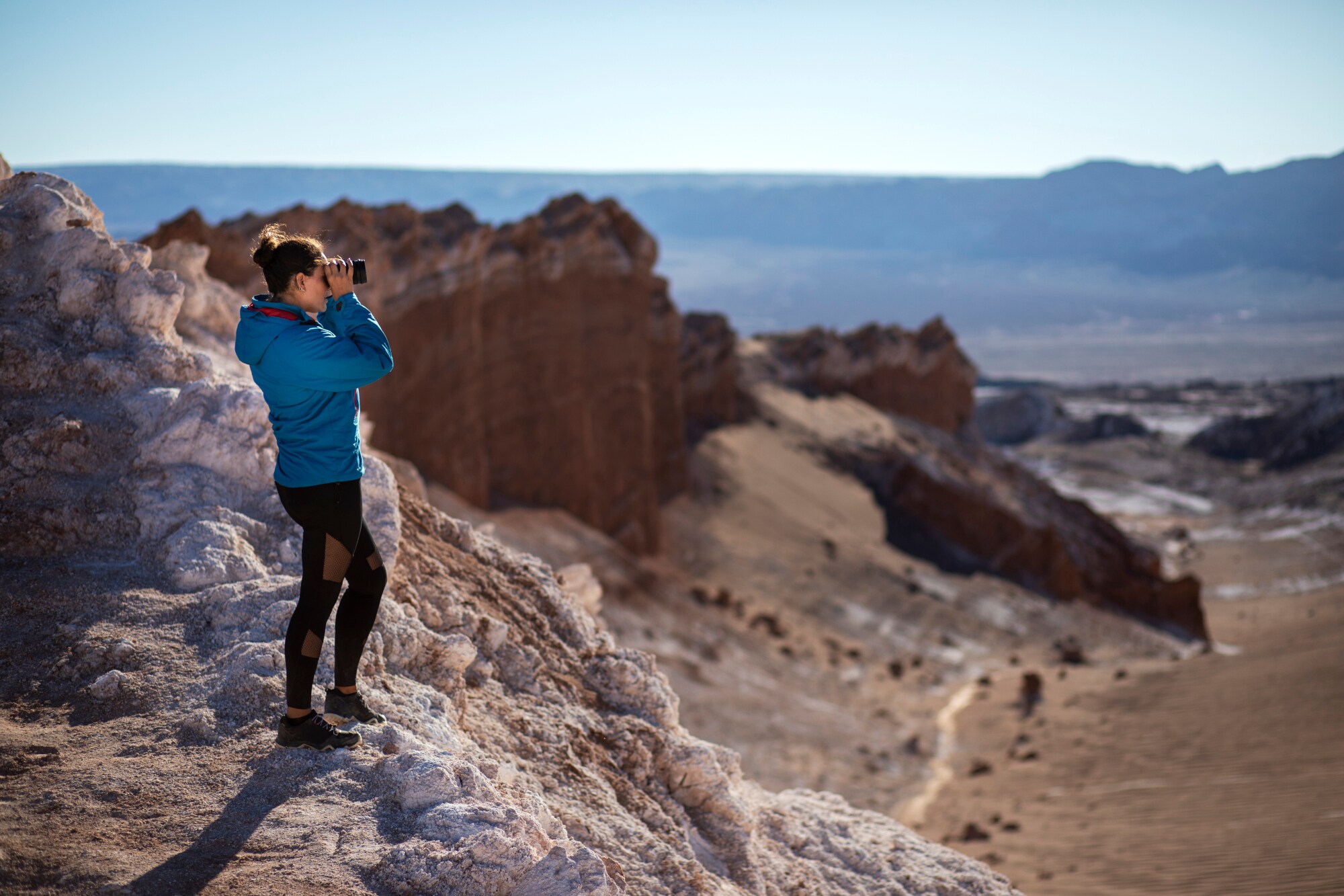 Eine junge Frau mit Fernglas steht auf einem Felsen Eine junge Frau mit Fernglas steht auf einem Felsen