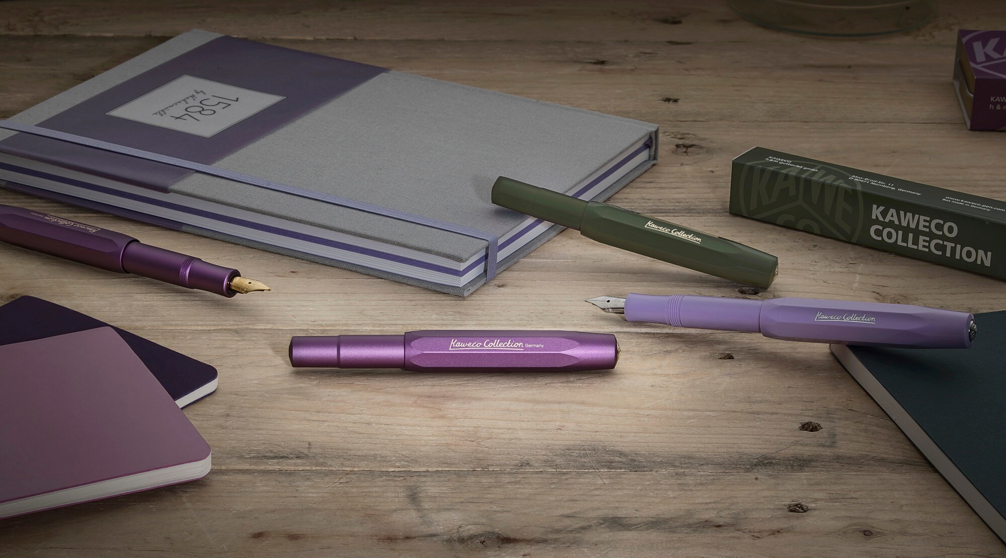 Mehrere Füllfederhalter liegen neben Notizbüchern auf einem Tisch verteilt Mehrere Füllfederhalter liegen neben Notizbüchern auf einem Tisch verteilt