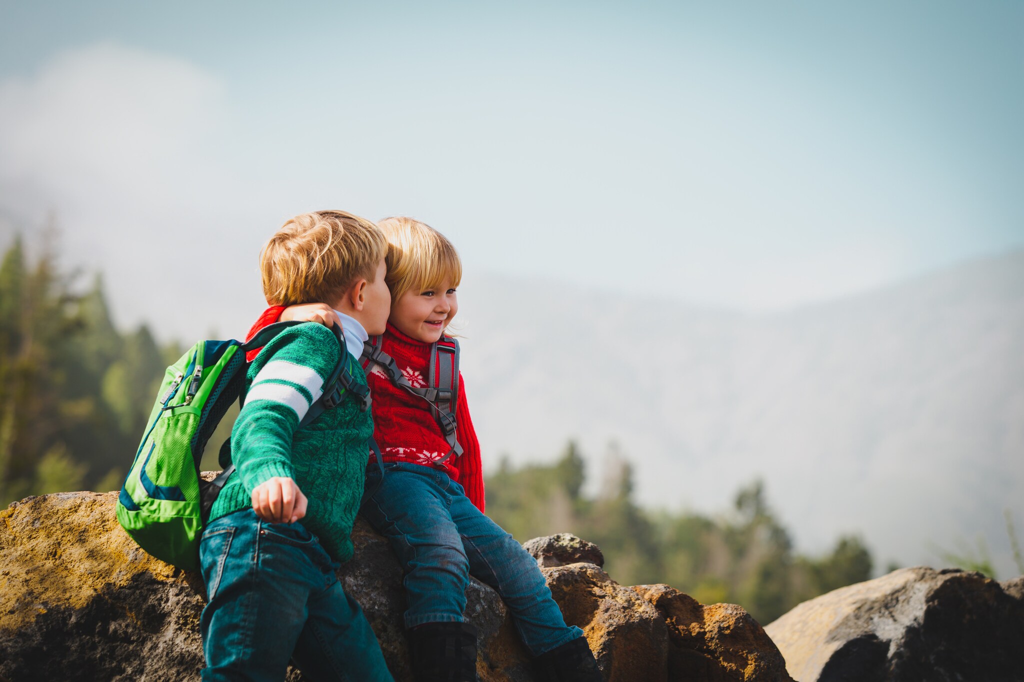 Zwei kleine fröhliche Kinder sitzen auf einem Stein vor Bergpanorama