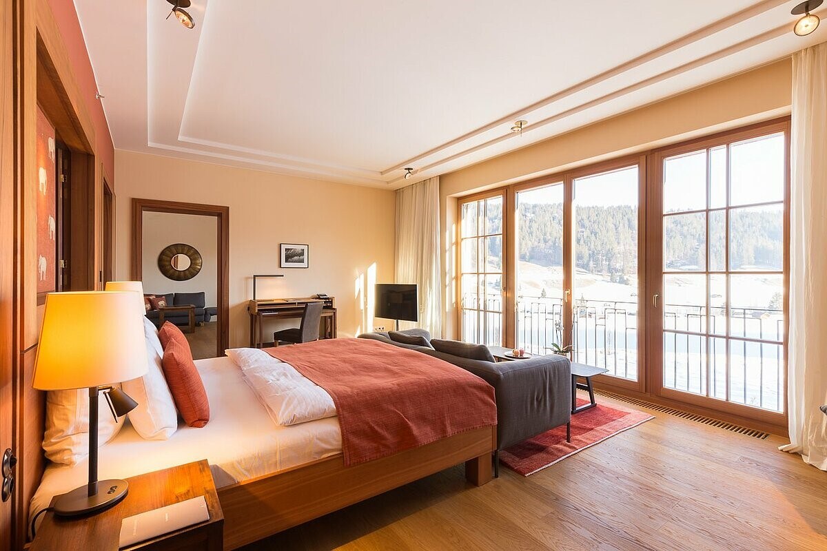 Großzügiges Hotelzimmer mit Doppelbett und Blick nach draußen durch die bodentiefen Fenster