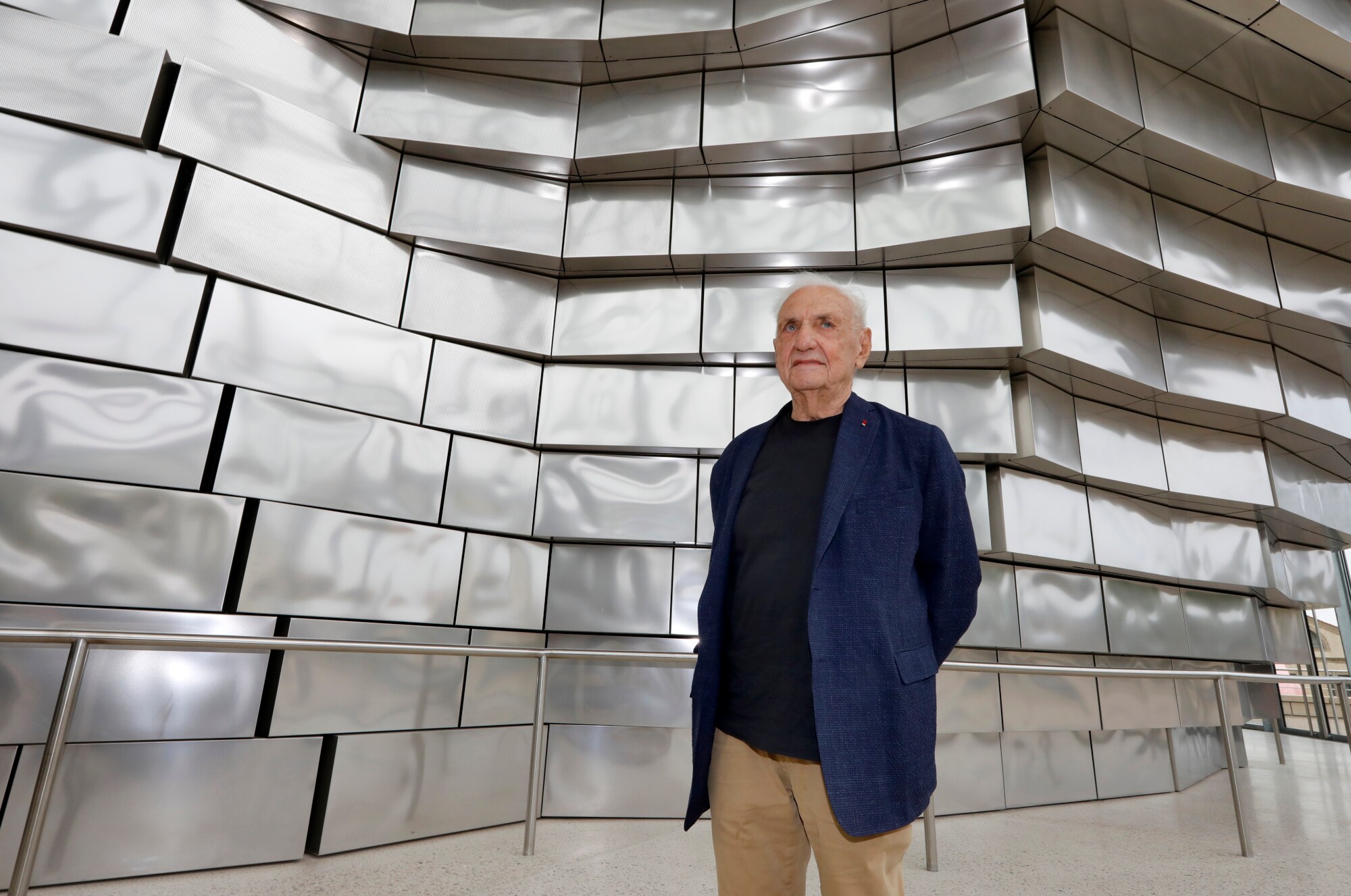 Architekt Frank Gehry vor einer Fassade aus glänzenden Aluminiumplatten