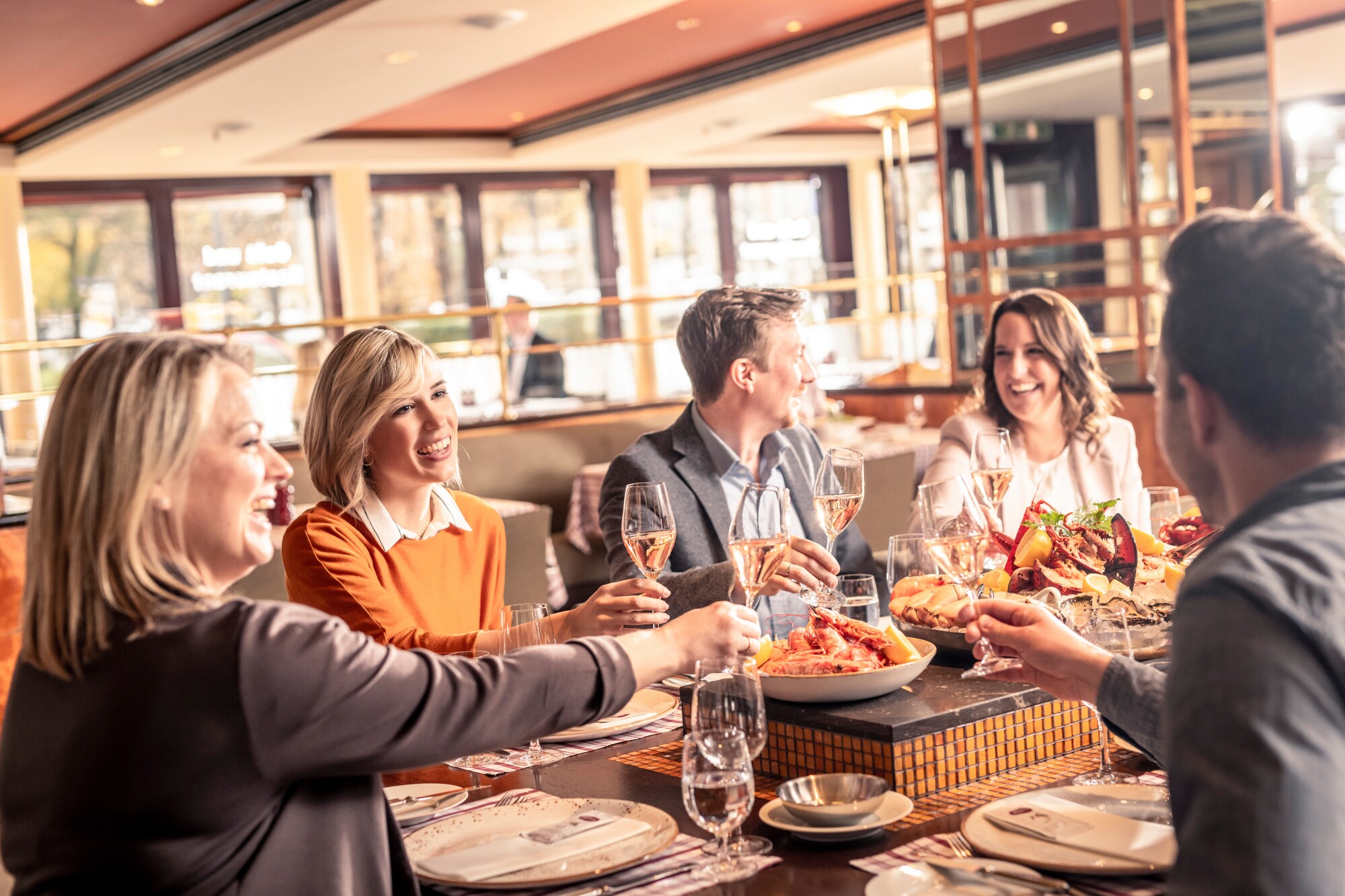 Mehrere gut gelaunte Personen stoßen mit einem Getränk an und essen Meeresfrüchte Mehrere gut gelaunte Personen stoßen mit einem Getränk an und essen Meeresfrüchte