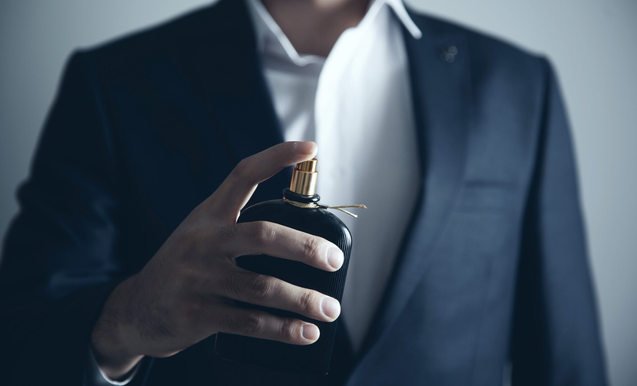 Eine männliche Hand hält einen dunklen Flakon mit goldfarbenem Verschluss vor den Oberkörper Eine männliche Hand hält einen dunklen Flakon mit goldfarbenem Verschluss vor den Oberkörper