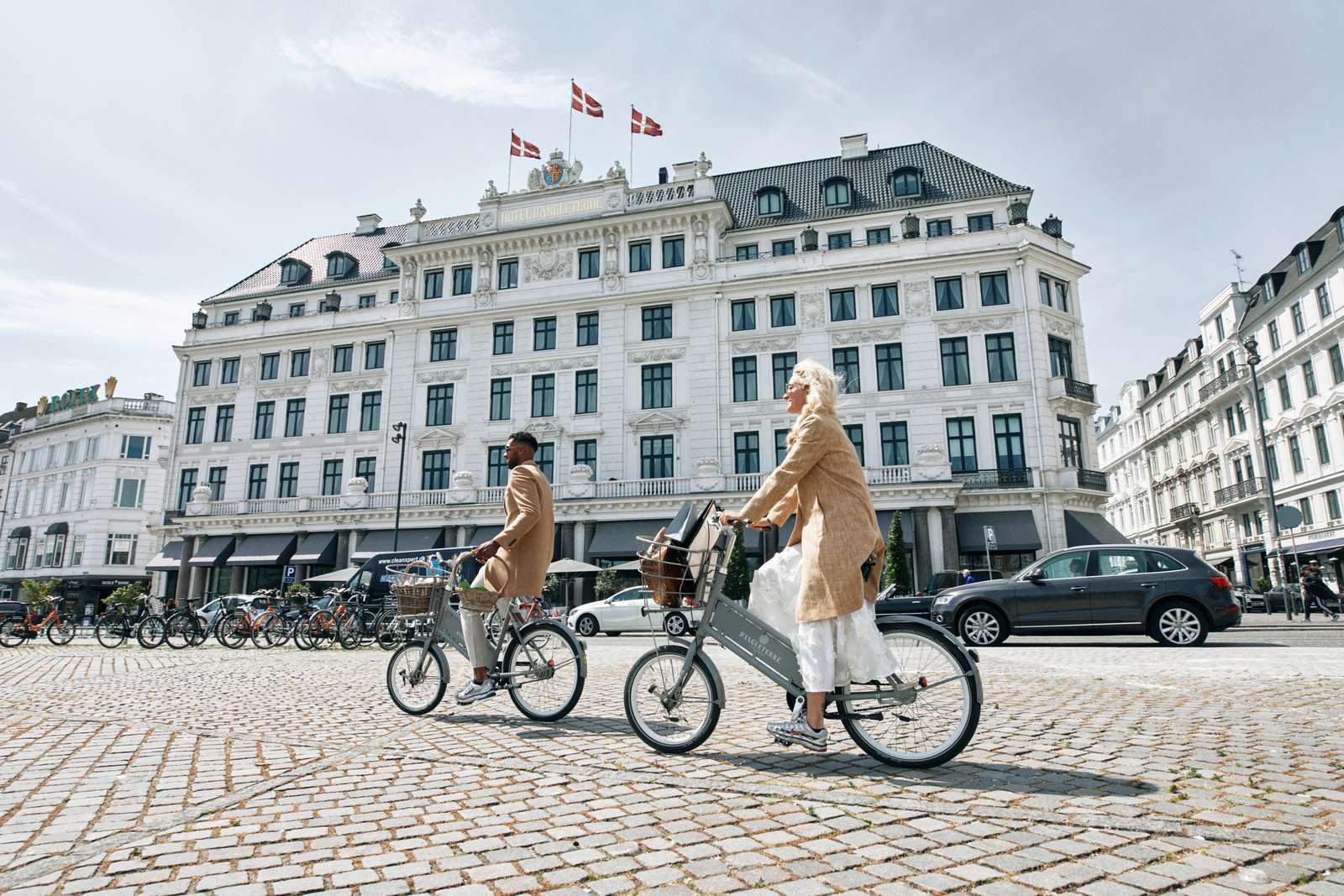 Zwei schick gekleidete Personen auf Fahrrädern vor dem neoklassizistischen Gebäude des Hotel d´Angleterre in Kopenhagen Zwei schick gekleidete Personen auf Fahrrädern vor dem neoklassizistischen Gebäude des Hotel d´Angleterre in Kopenhagen