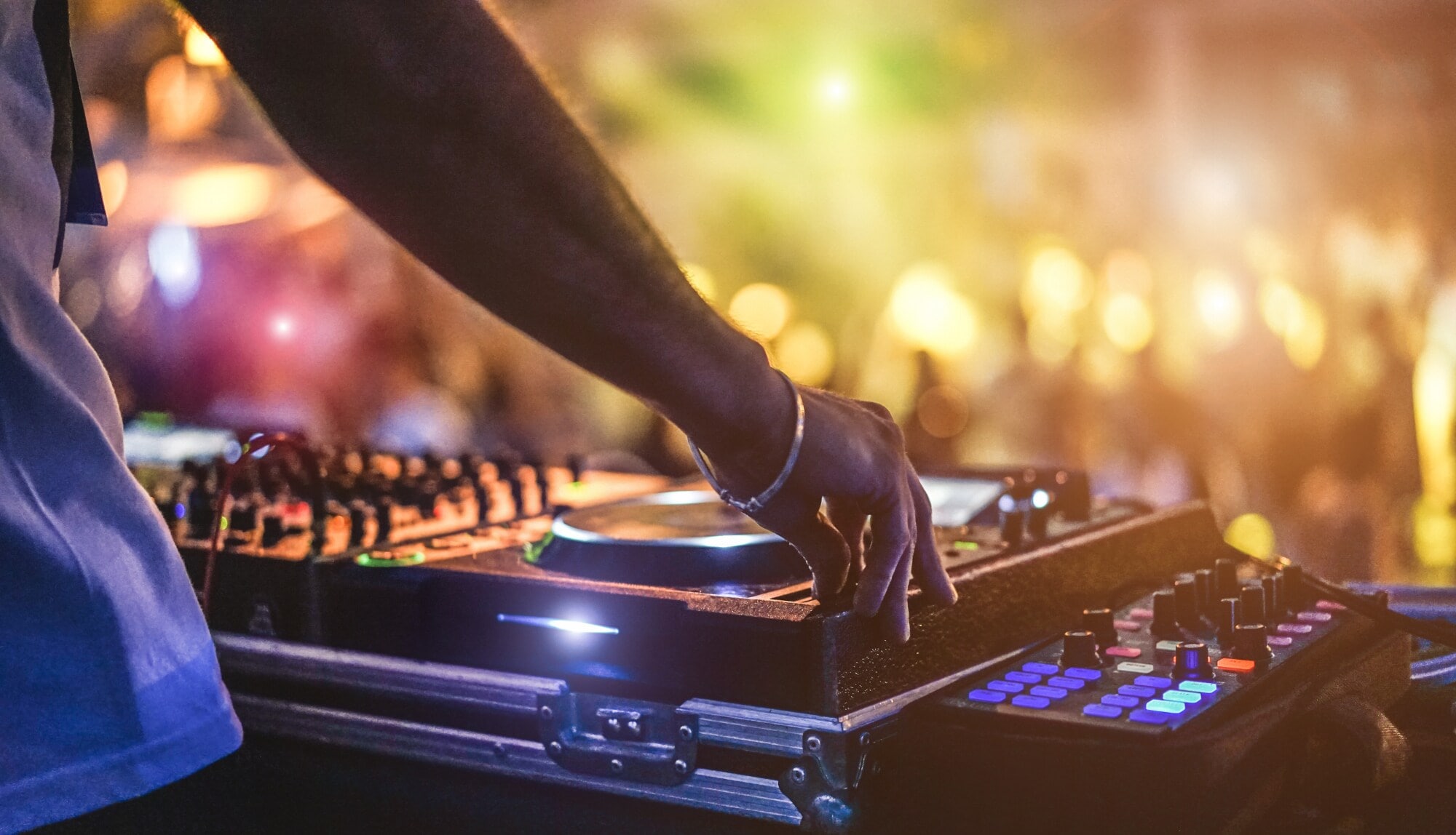 Die Hand eines DJs am Mischpult auf einem Festival mit Menschenmenge im Hintergrund Die Hand eines DJs am Mischpult auf einem Festival mit Menschenmenge im Hintergrund