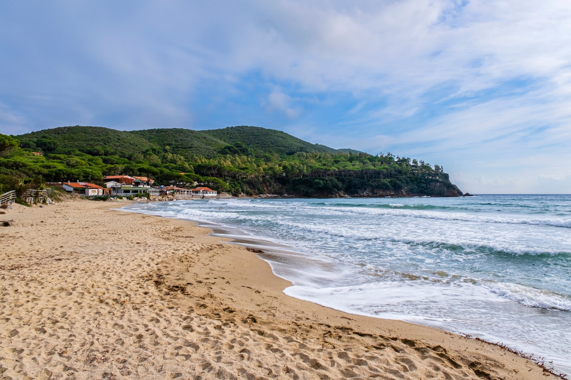 Ein leerer Strand, im Hintergrund ein grünes Wäldchen und eine kleine Siedlung Ein leerer Strand, im Hintergrund ein grünes Wäldchen und eine kleine Siedlung