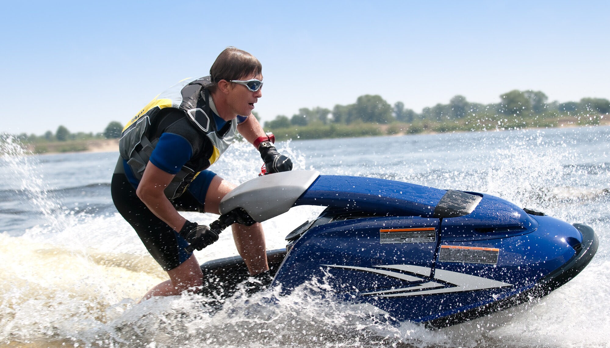 Ein Mann fährt in Neoprenanzug, Schwimmweste und Brille einen Jetski