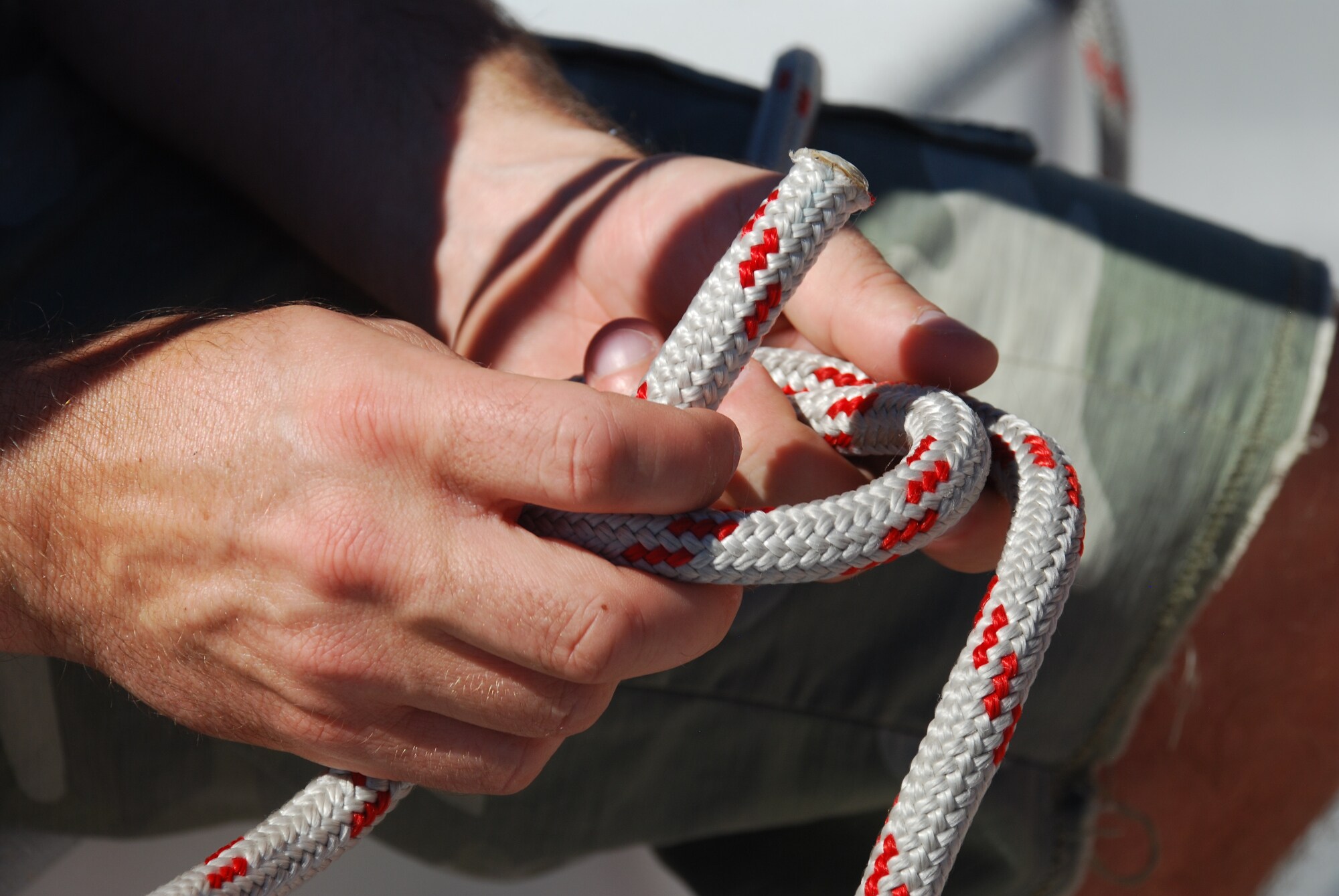 Zwei Hände, die ein weiß-rotes Seil zum Knoten schnüren