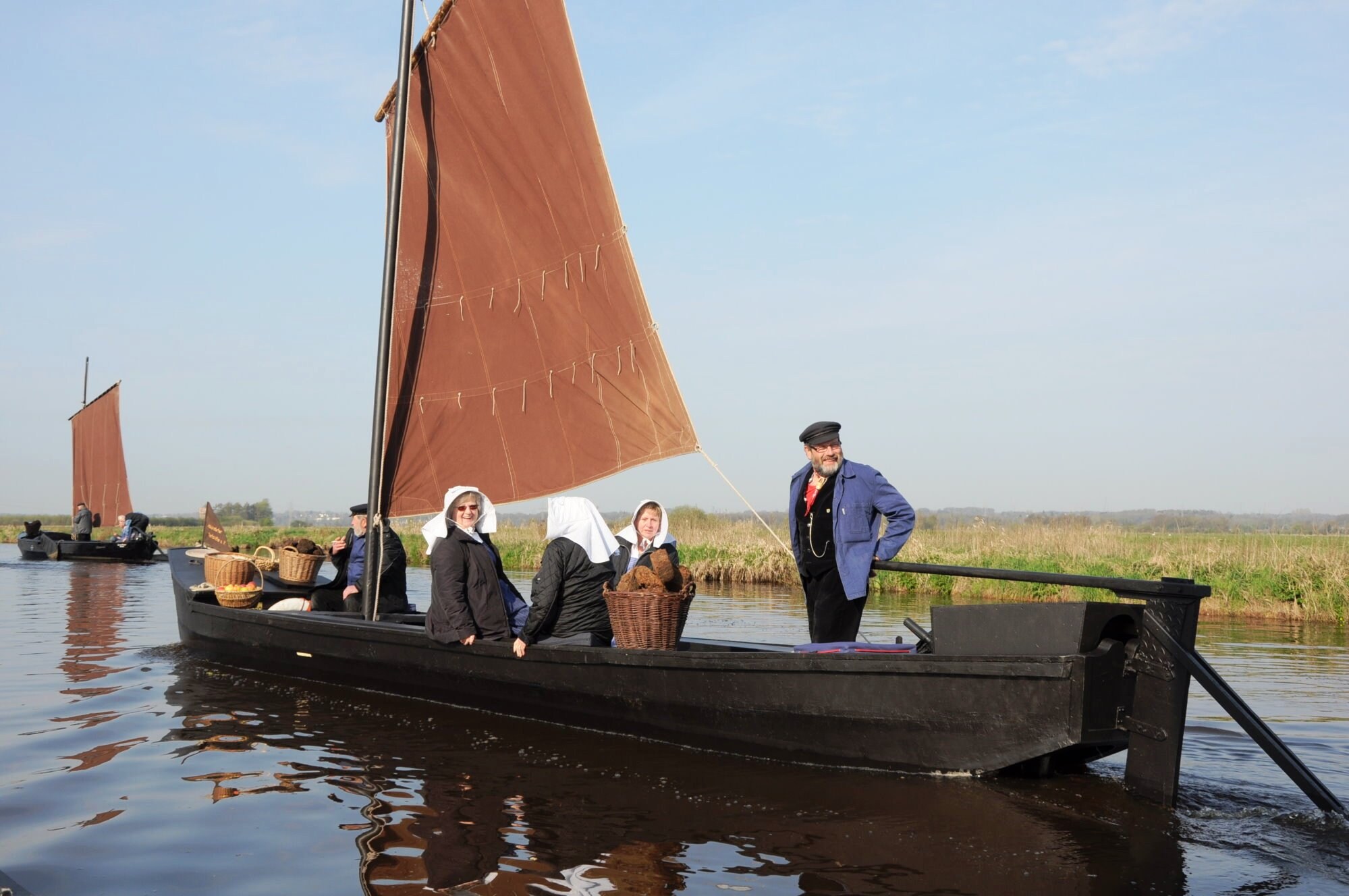 Kleines Holzschiff mit Stoffsegel und fünf Passagieren schippert über einen kleinen Fluss