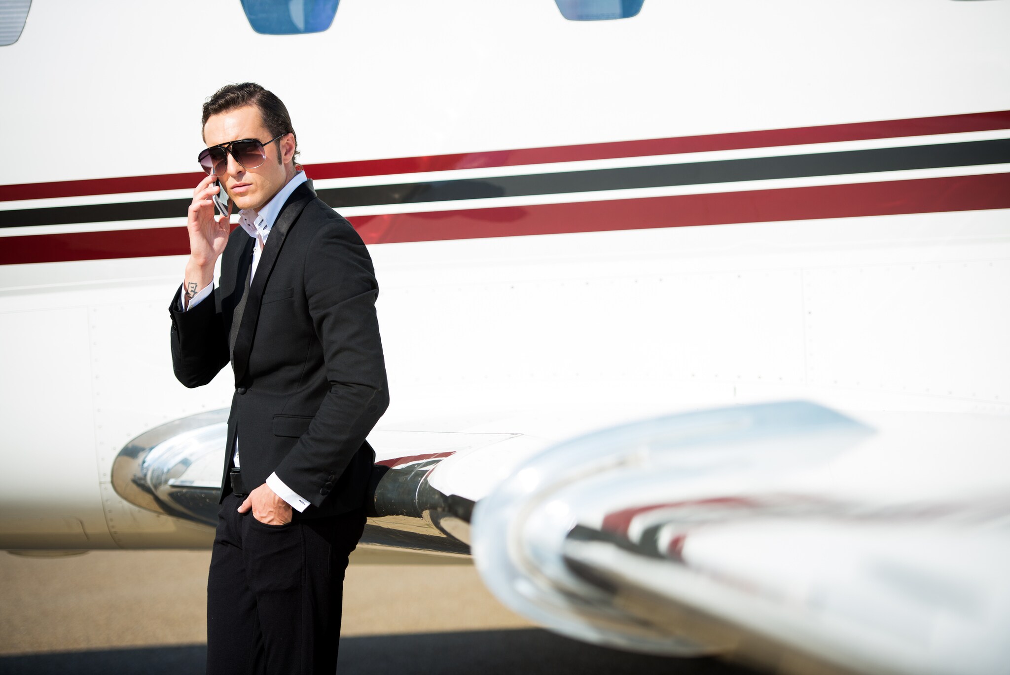 Junger Geschäftsmann neben dem Privatjet-Flugzeug, der mit seinem Smartphone telefoniert.