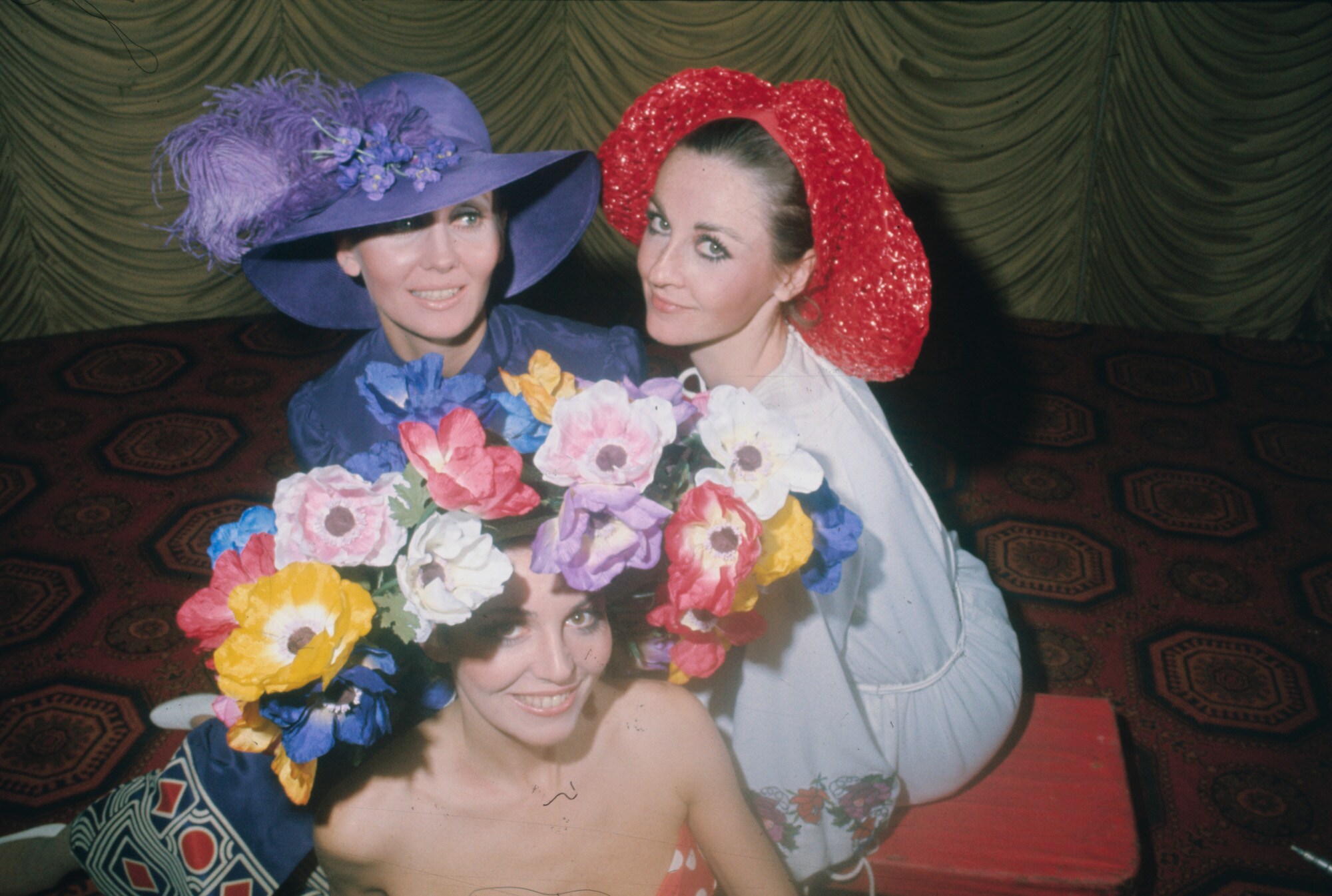 Drei weibliche Models mit auffälligen Hutkreationen