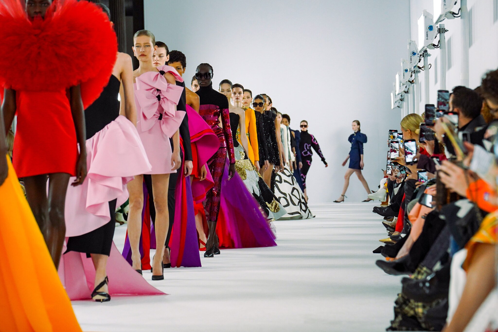 Eine Reihe weiblicher Models in bunten Abendkleidern vor Publikum auf einem Laufsteg