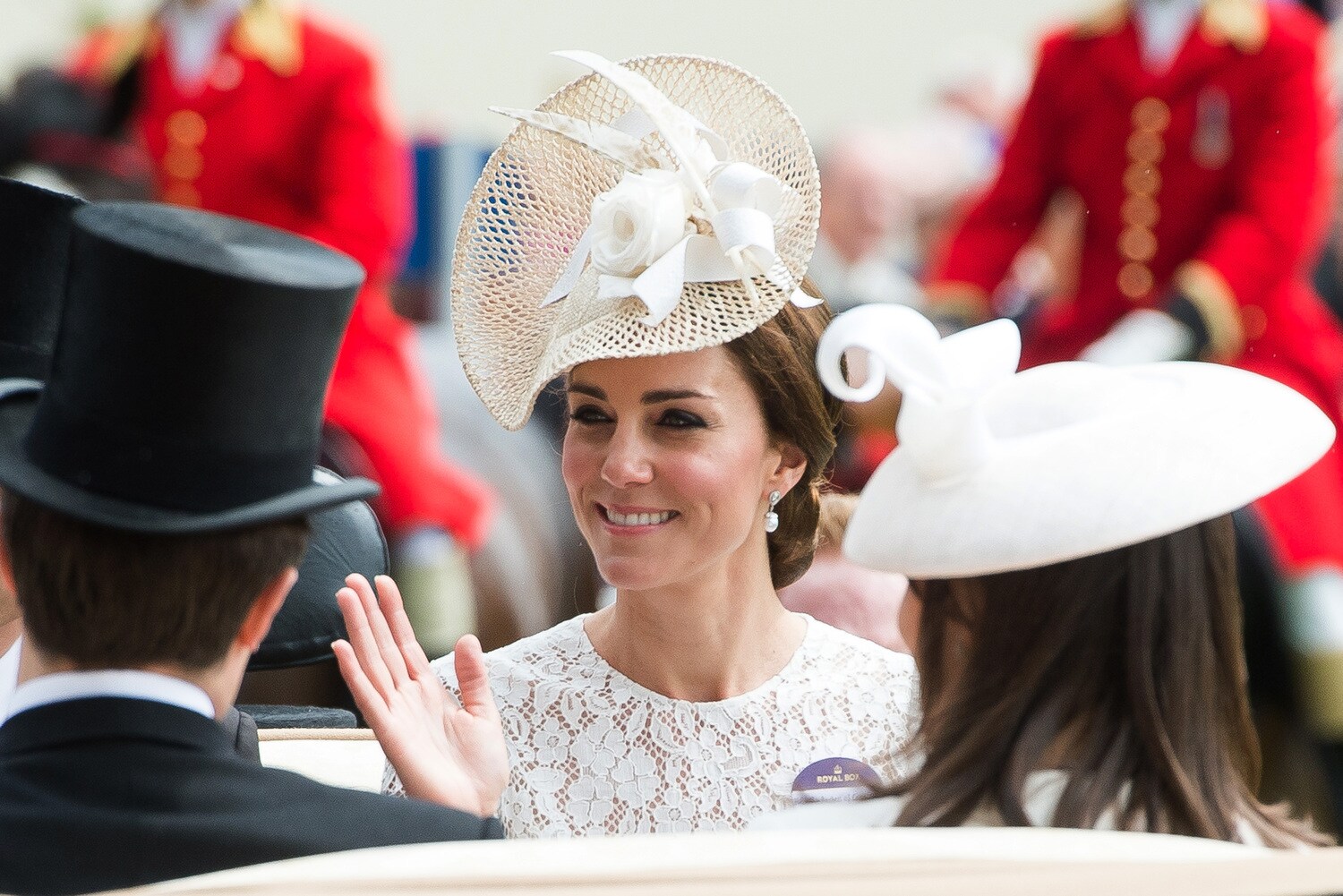 Nahaufnahme von Herzogin Catherine, die mit einem eleganten, weißen Fascinator auf dem Kopf aus einer Kutsche winkt