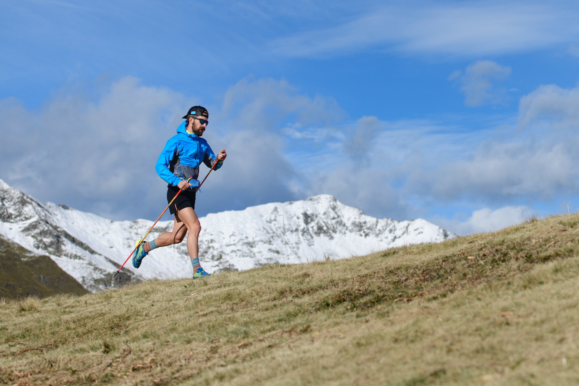 Ein Mann rennt bei bestem Wetter in einem bergigen Gebiet und nutzt dabei Laufstöcker