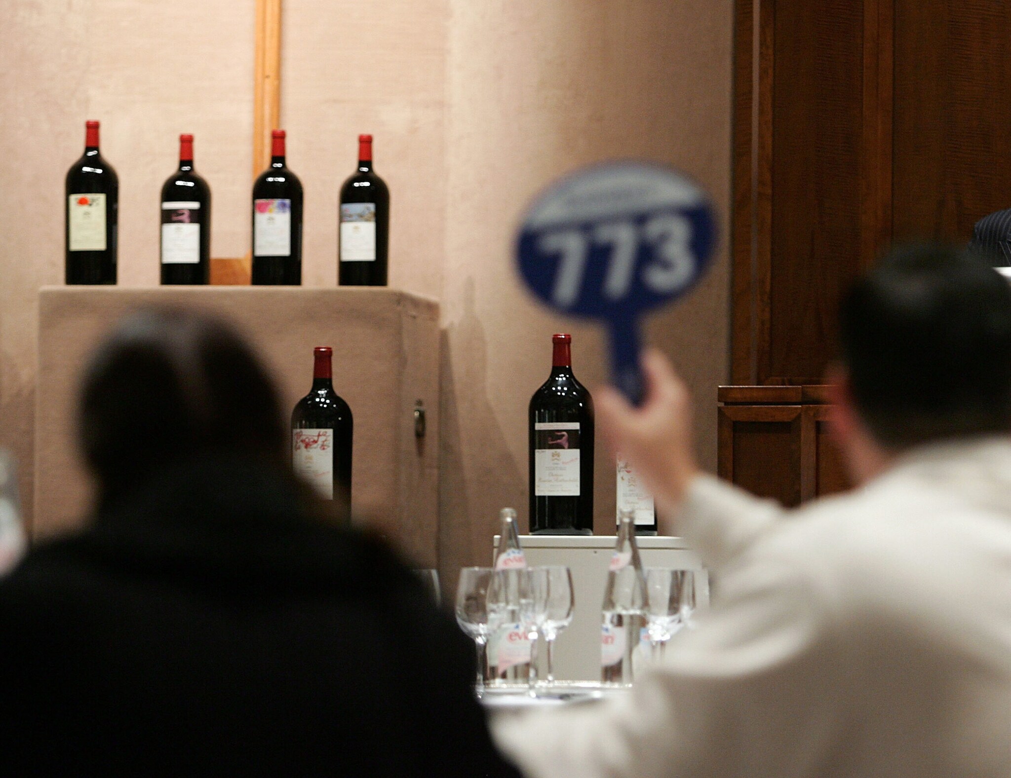 Käufer bei einer Auktion bieten mit Nummernschildern auf Rotweinflaschen der Marke Chateau Mouton Rothschild