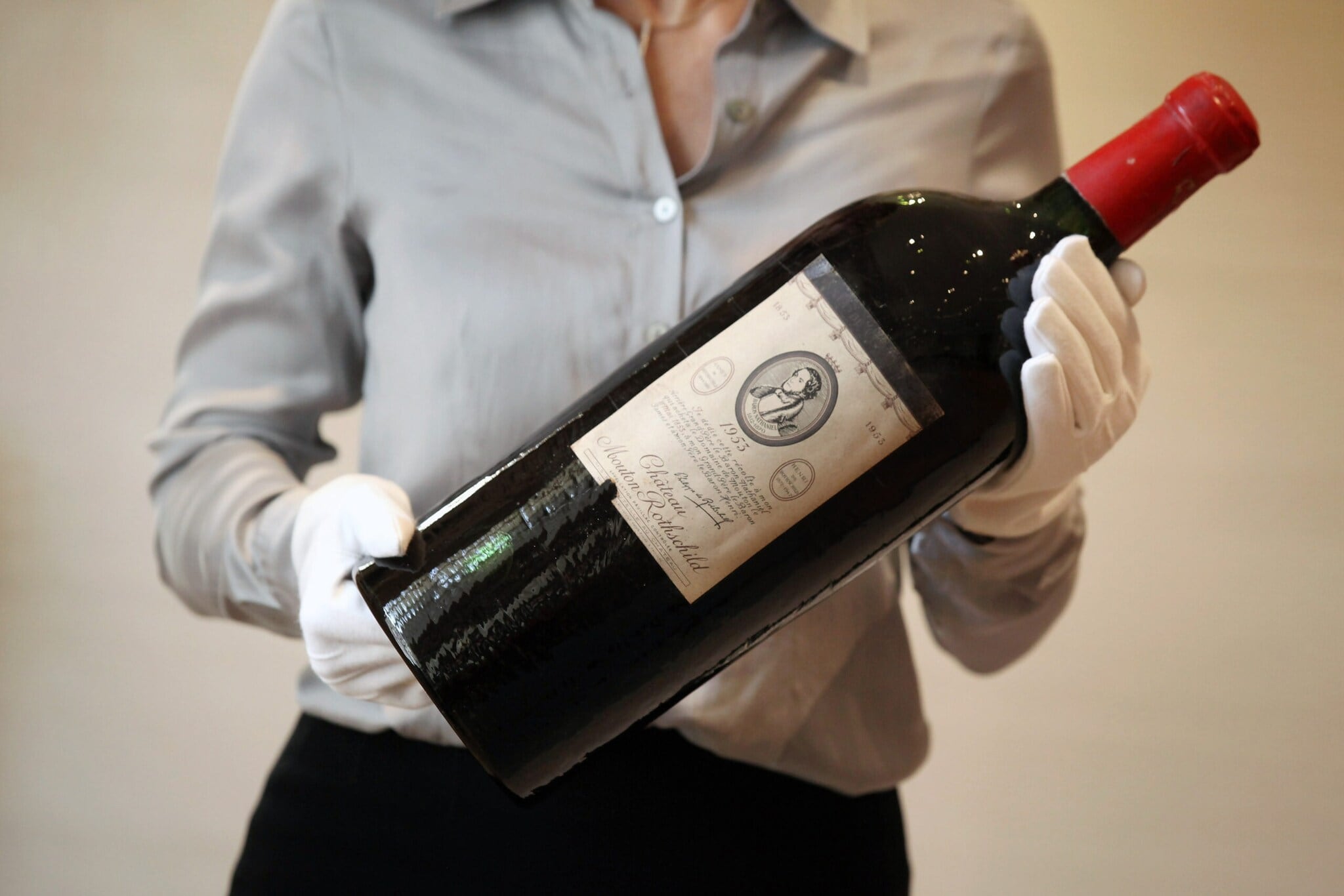 Eine große Flasche Rotwein der Marke Chateau Mouton Rothschild wir von einer Person mit weißen Handschuhen gehalten Eine große Flasche Rotwein der Marke Chateau Mouton Rothschild wir von einer Person mit weißen Handschuhen gehalten