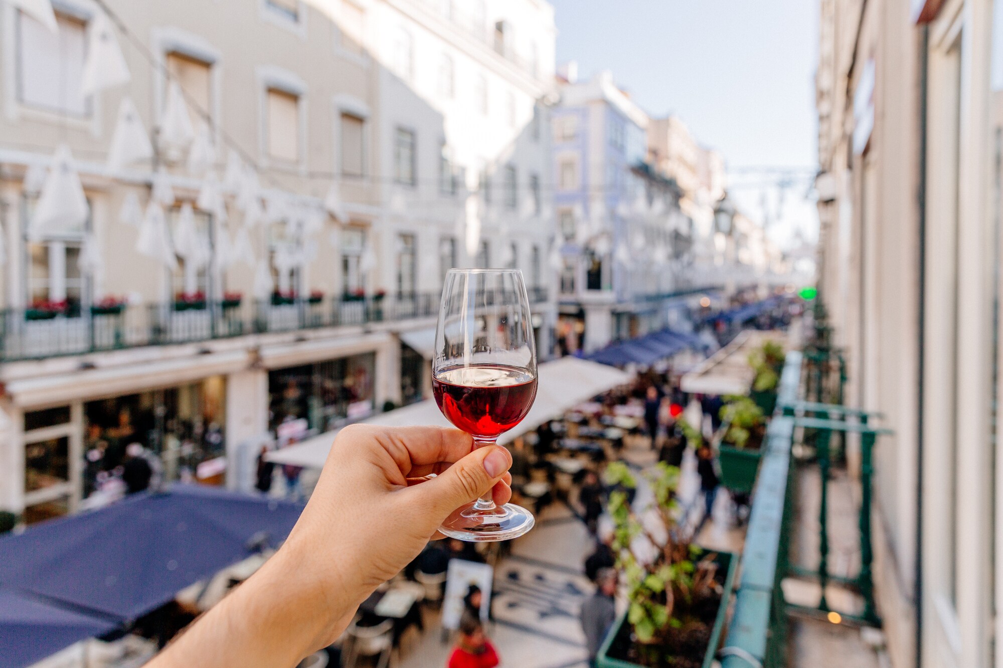 Eine Hand hält ein Glas Portwein oberhalb einer belebten Gasse in die Luft Eine Hand hält ein Glas Portwein oberhalb einer belebten Gasse in die Luft