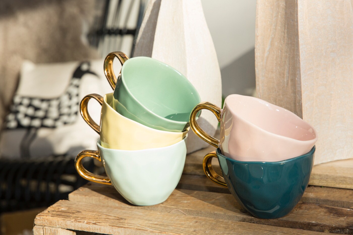 Bunte Tassen mit goldenem Henkel stehen ineinandergestapelt auf einer Holzkiste