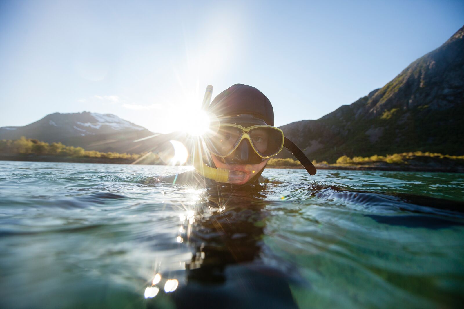 Ein Taucher mit Taucherbrille und Schnorchel taucht aus dem Wasser auf